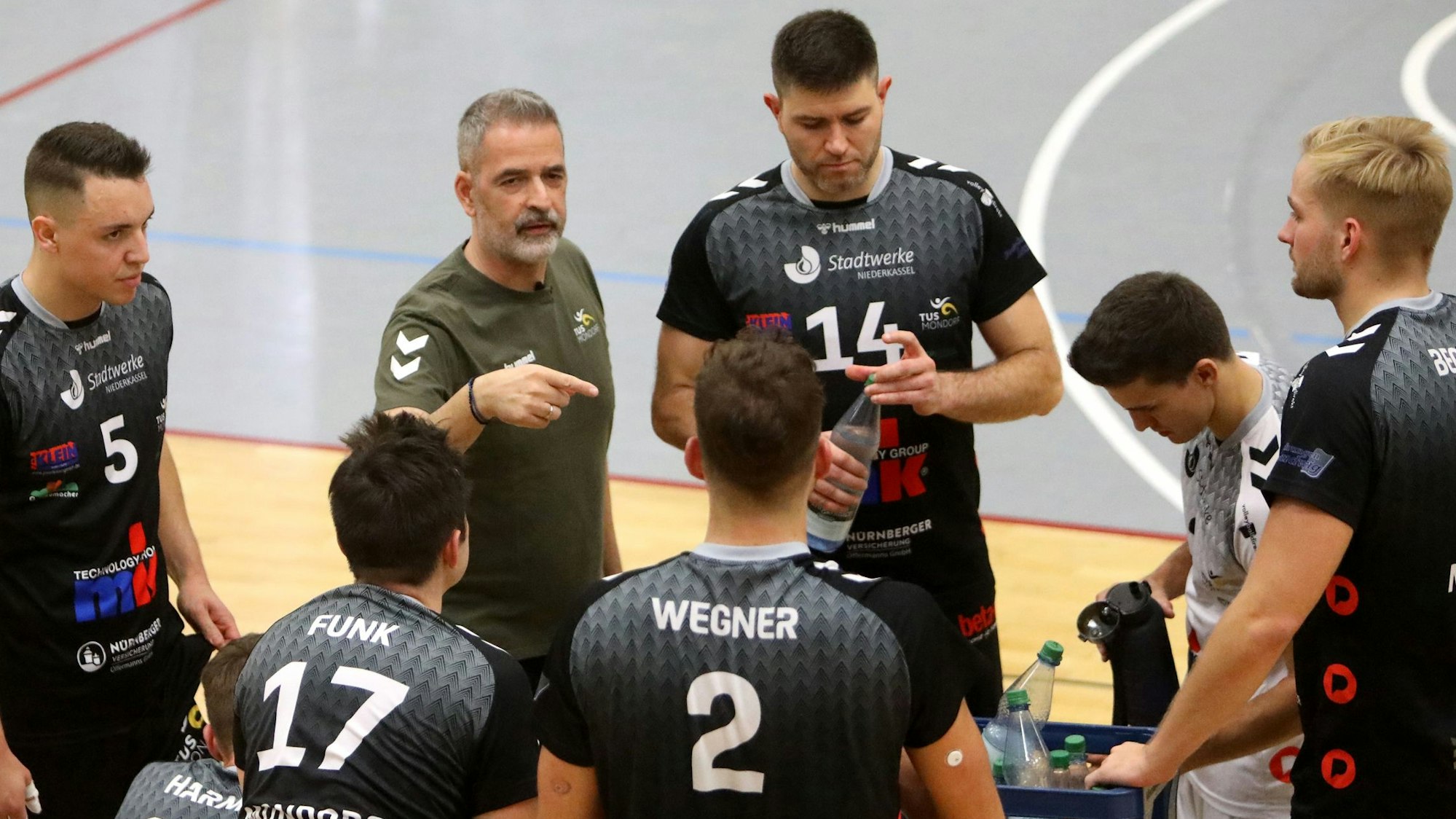 Cheftrainer Tasos Vlasakidis vom TuS Mondorf macht Ansagen und gestikuliert, seine Spieler hören gespannt zu.