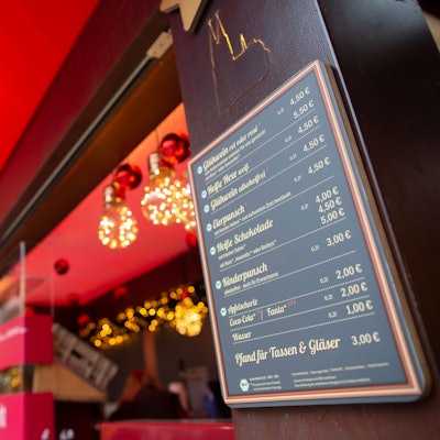 Auf einer Preistafel auf dem Weihnachtsmarkt auf dem Roncalliplatz stehen Preise für Glühwein und Co.