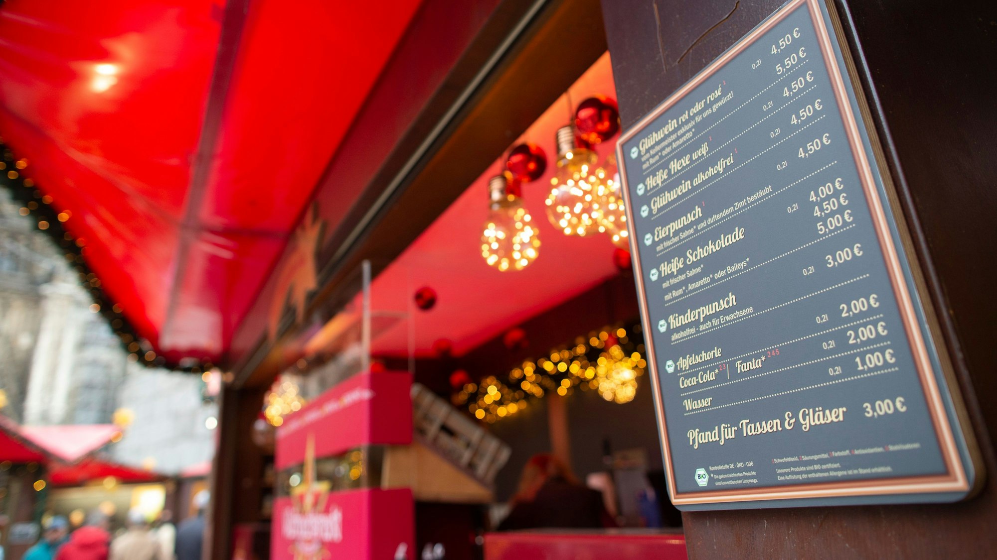Auf einer Preistafel auf dem Weihnachtsmarkt auf dem Roncalliplatz stehen Preise für Glühwein und Co.