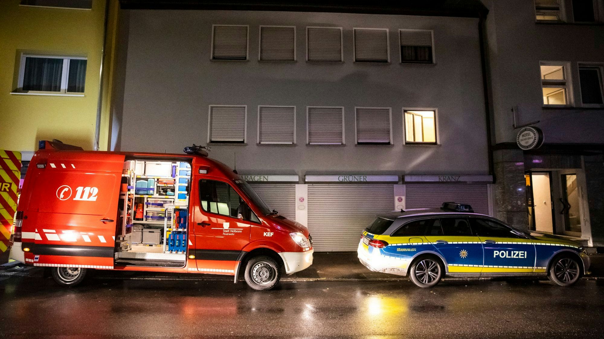 Je ein Fahrzeug der Feuerwehr und der Polizei stehen während eines Großeinsatzes nachts vor einer städtischen Häuserreihe.