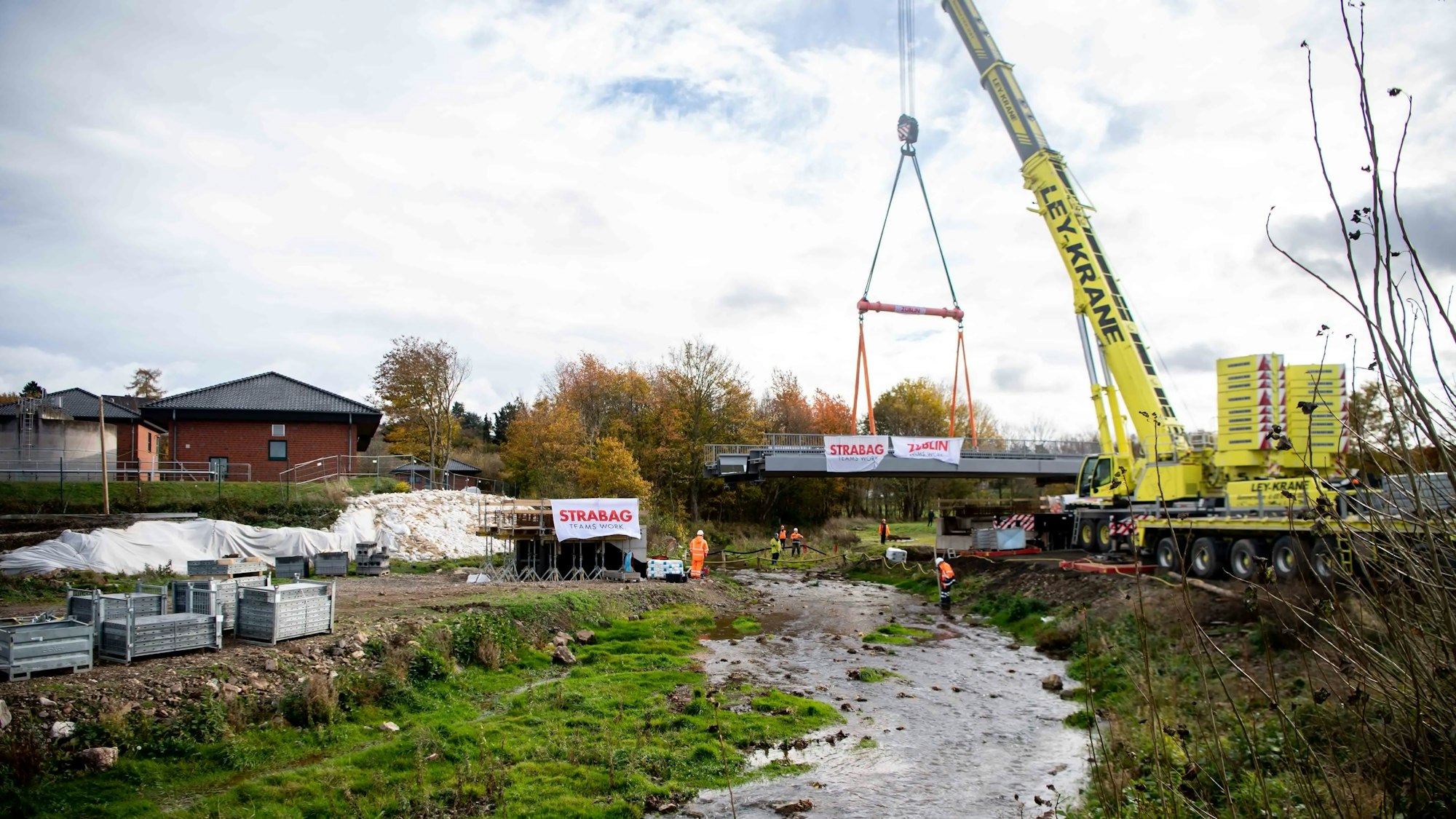 Ein gelber Kran hebt eine Brücke über die Erft.
