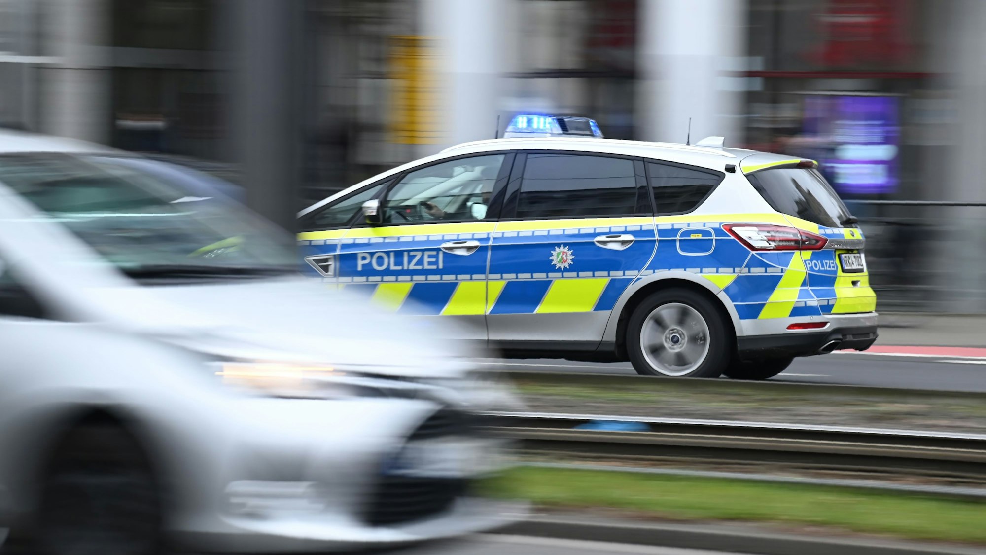Ein Polizeiwagen im Einsatz auf einer Straße in der Stadt. Zwischen den Straßenspuren verlaufen Stadtbahnschienen.