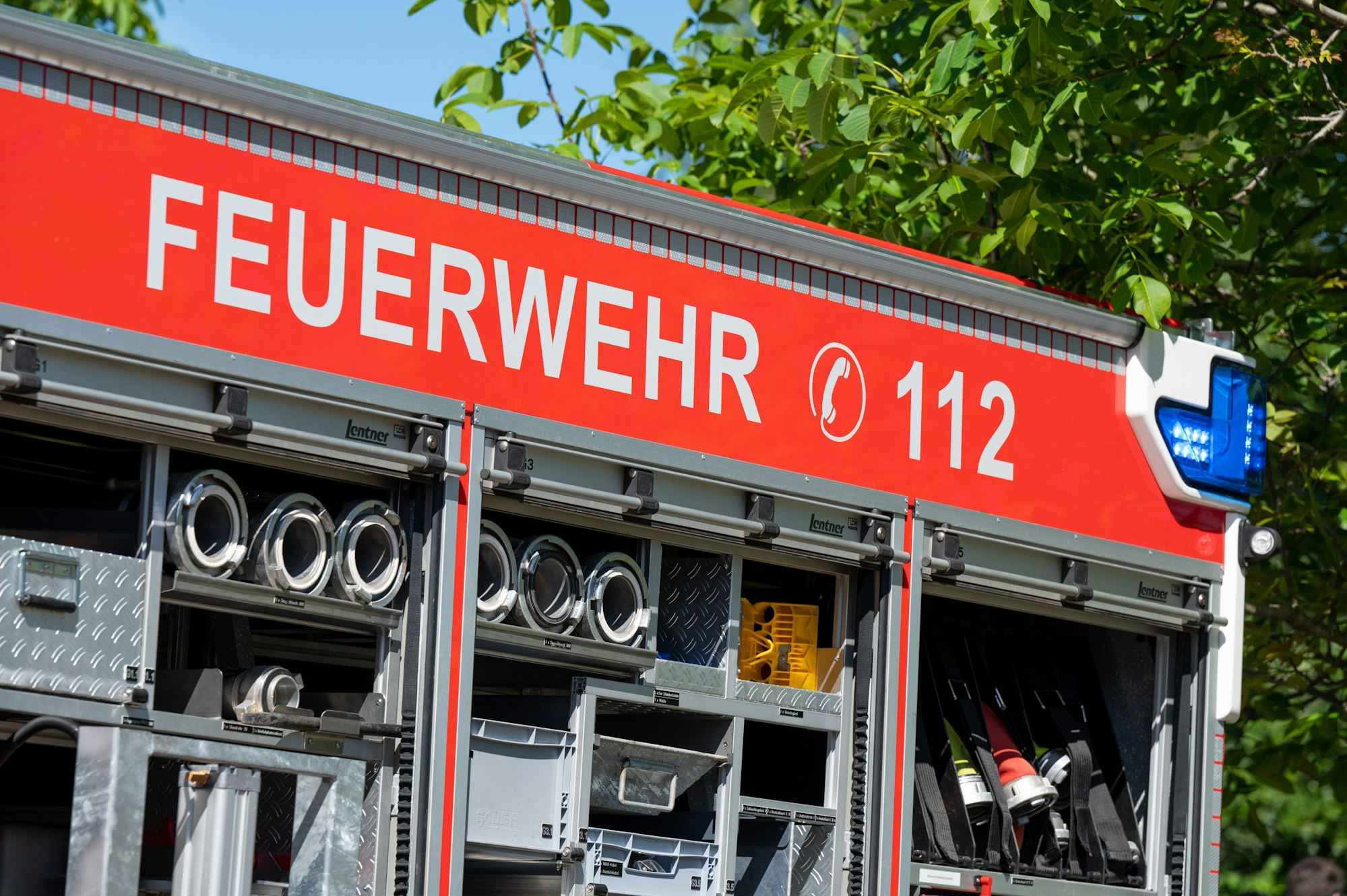 Großaufnahme eines Feuerwehr-Autos. In weißen Lettern steht auf rotem Grund „Feuerwehr 112“. Es sind außerdem einige Schläuche und Gerätschaften zu sehen.