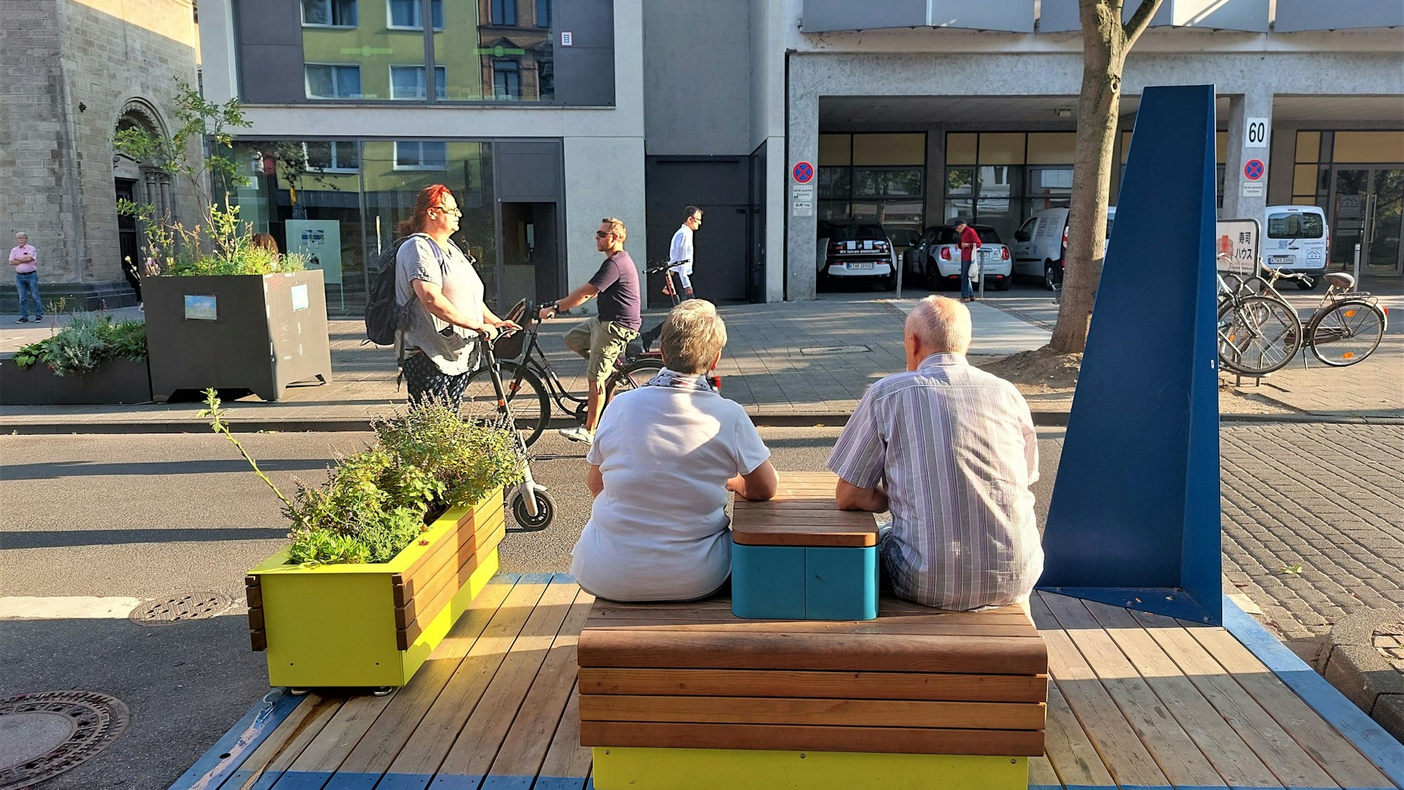 Zwei ältere Menschen sitzen auf einer Holzbank an der Deutzer Freiheit.