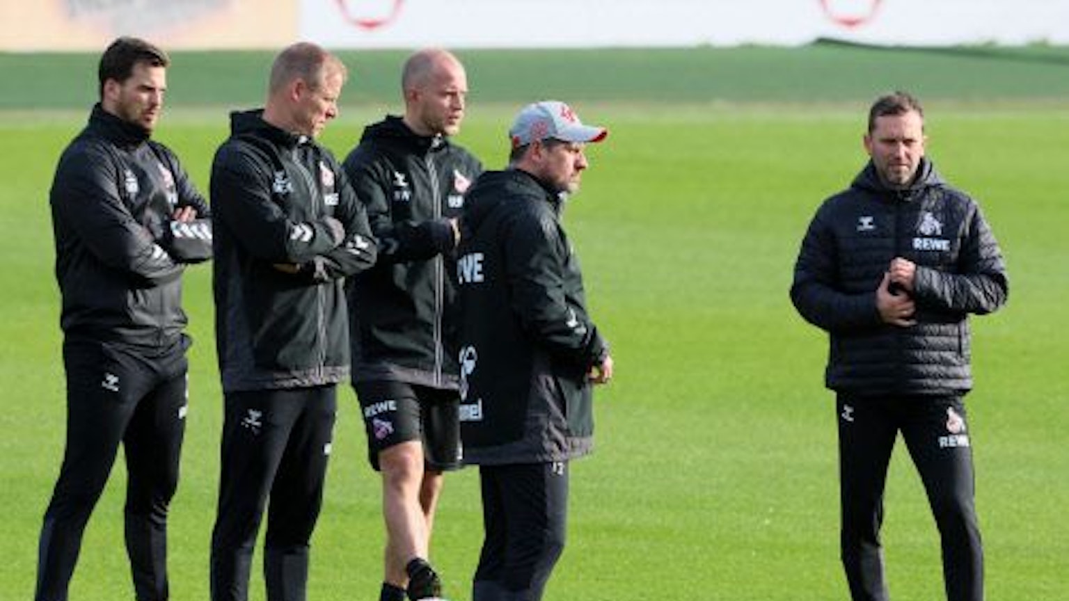 Das Trainerteam des 1. FC Köln mit Cheftrainer Steffen Baumgart steht auf dem Platz und schaut bei den Übungen der Spieler zu.
