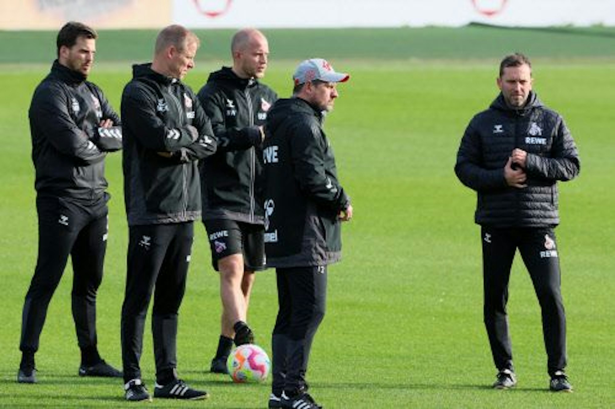 Das Trainerteam des 1. FC Köln mit Cheftrainer Steffen Baumgart steht auf dem Platz und schaut bei den Übungen der Spieler zu.
