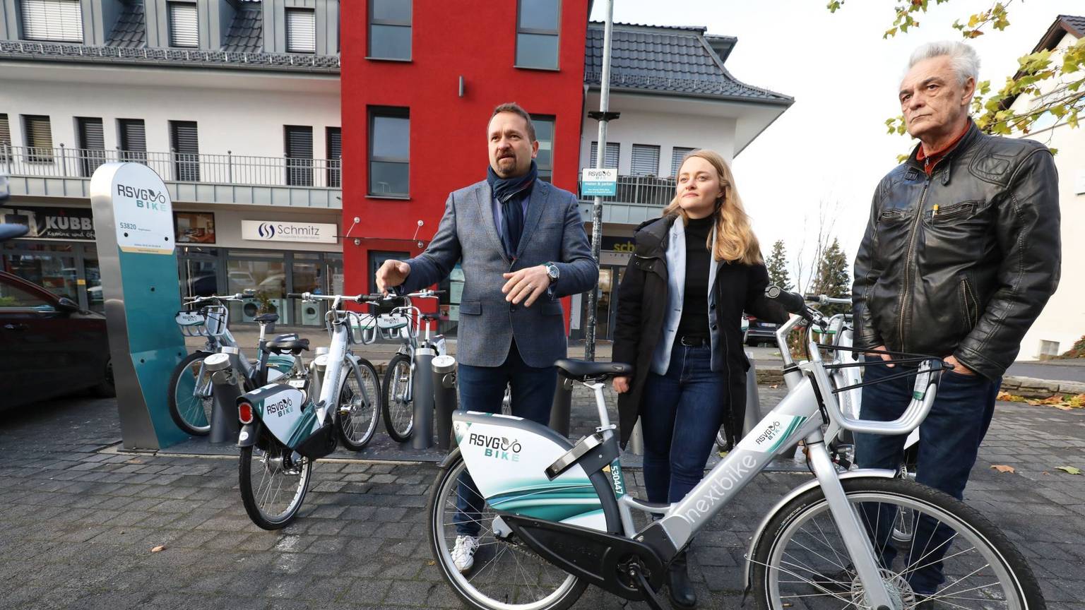 Eine Frau und zwei Männer – Holger Heuser, Kathrin Schmidt und Uwe Weingarten – stehen vor einer Ladestation für E-Bikes und zeigen eines der Fahrräder.