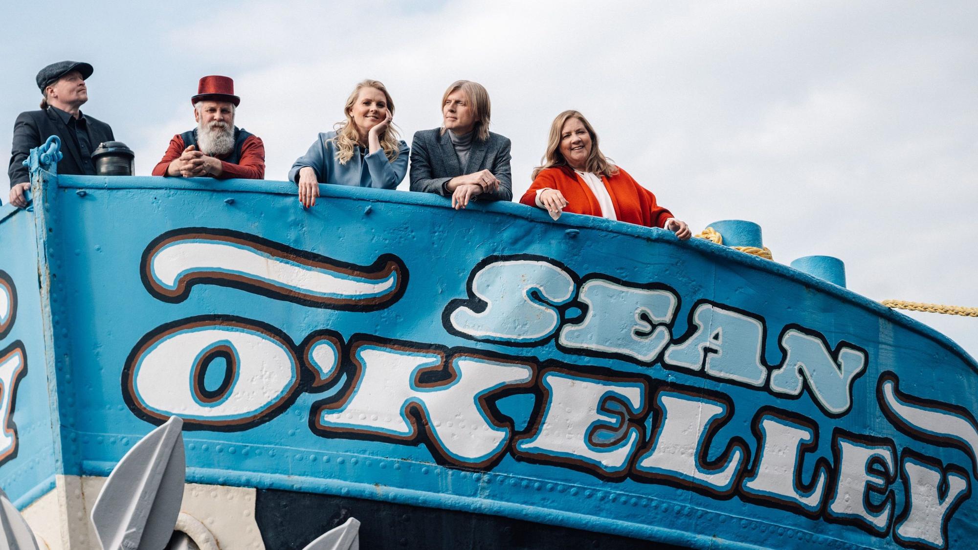 Man sieht Joey, Paul, Patricia, John und Kathy Kelly auf einem Boot. Das Boot ist blau angestrichen und hat den Schriftzug „Sean O´Kelly“. Im Hintergund sieht man den Himmel.