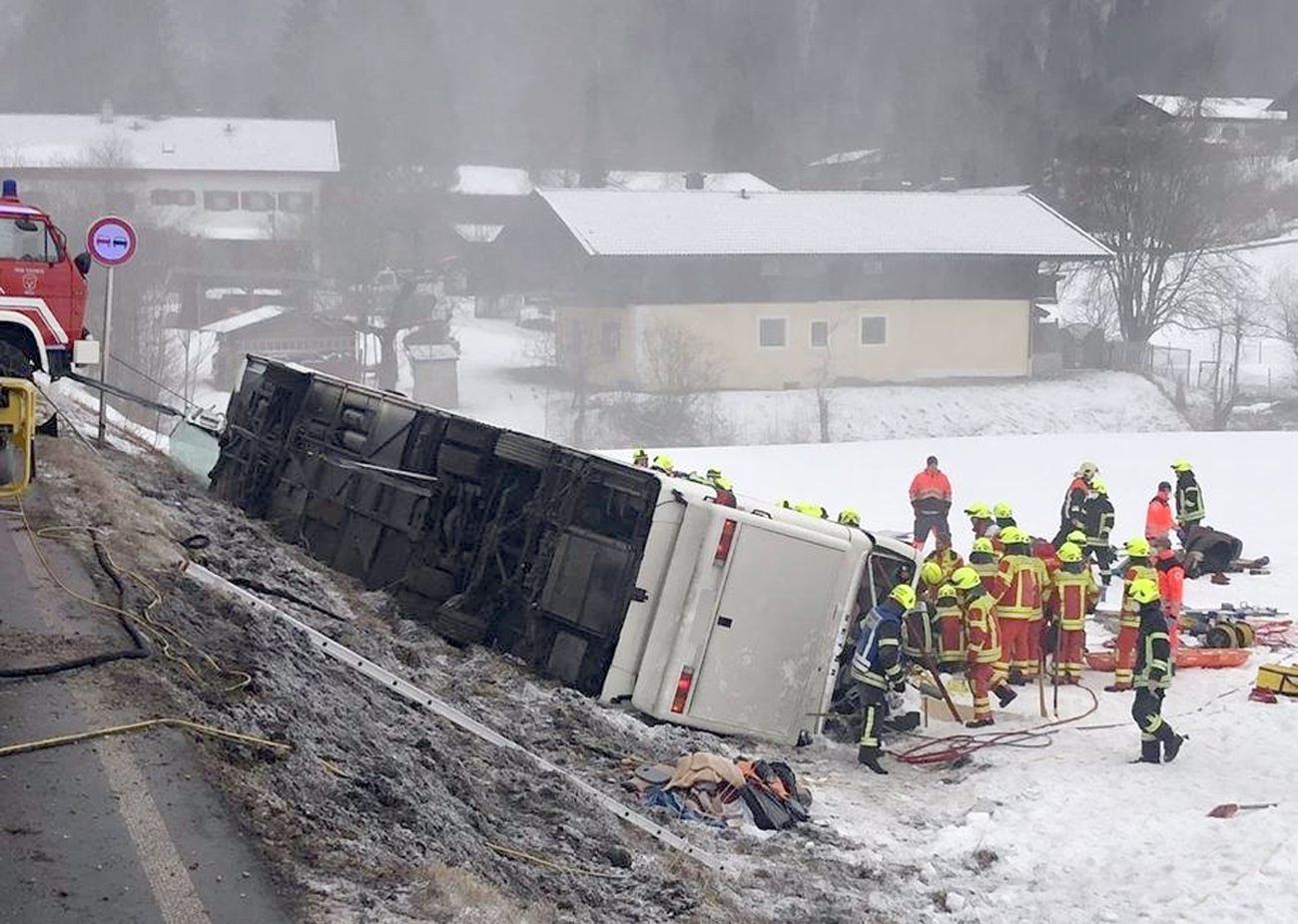 Einsatzkräfte der Feuerwehr stehen auf der Bundesstraße B306 am Ortsausgang von Inzell neben einem umgekippten Reisebus am Straßenrand.