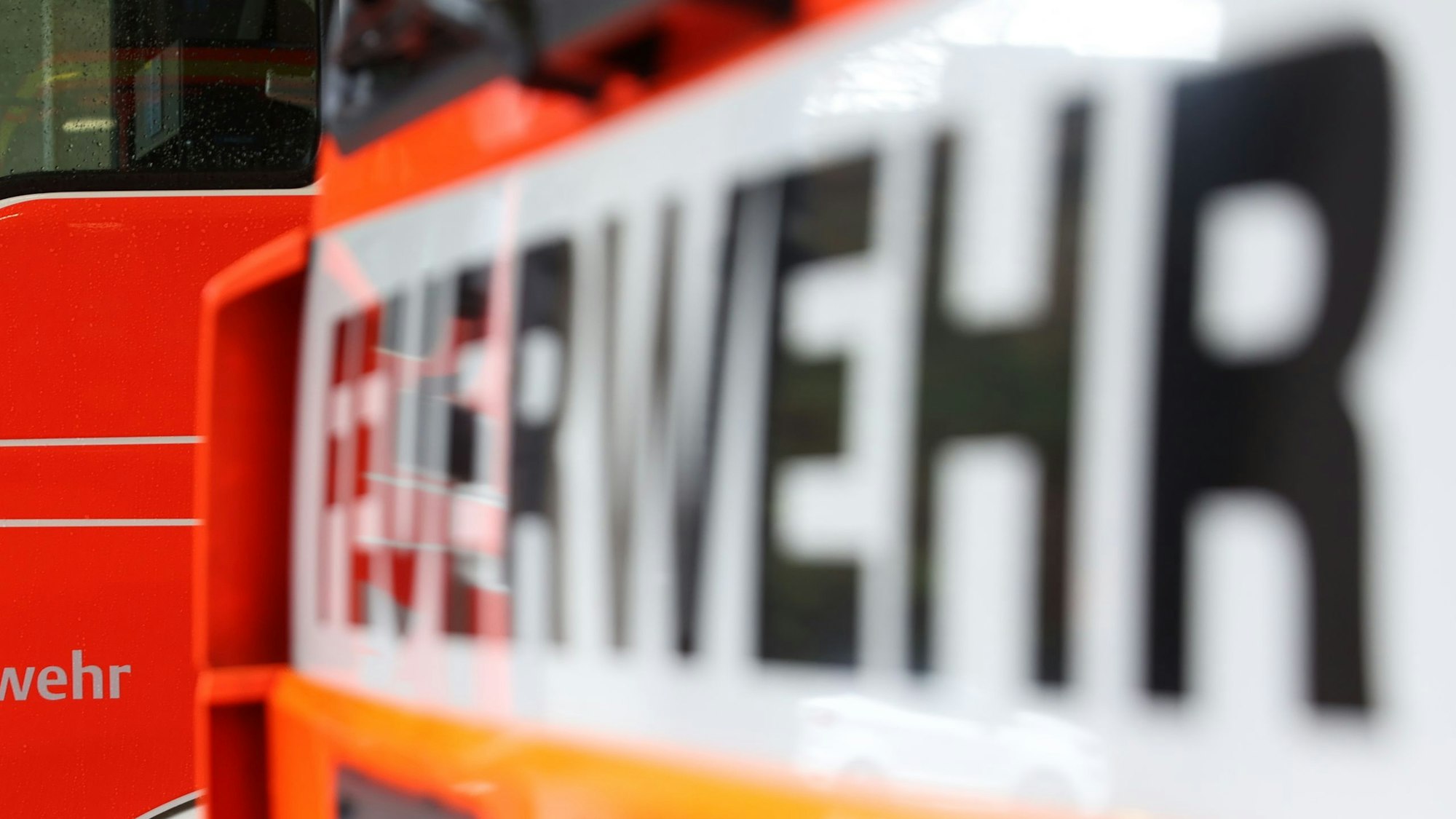 Man sieht die Front eines Feuerwehrwagens, samt Aufdruck. Der Schriftzug ist unscharf. Im Hintergrund sieht man ein anderes Feuerwehrauto.