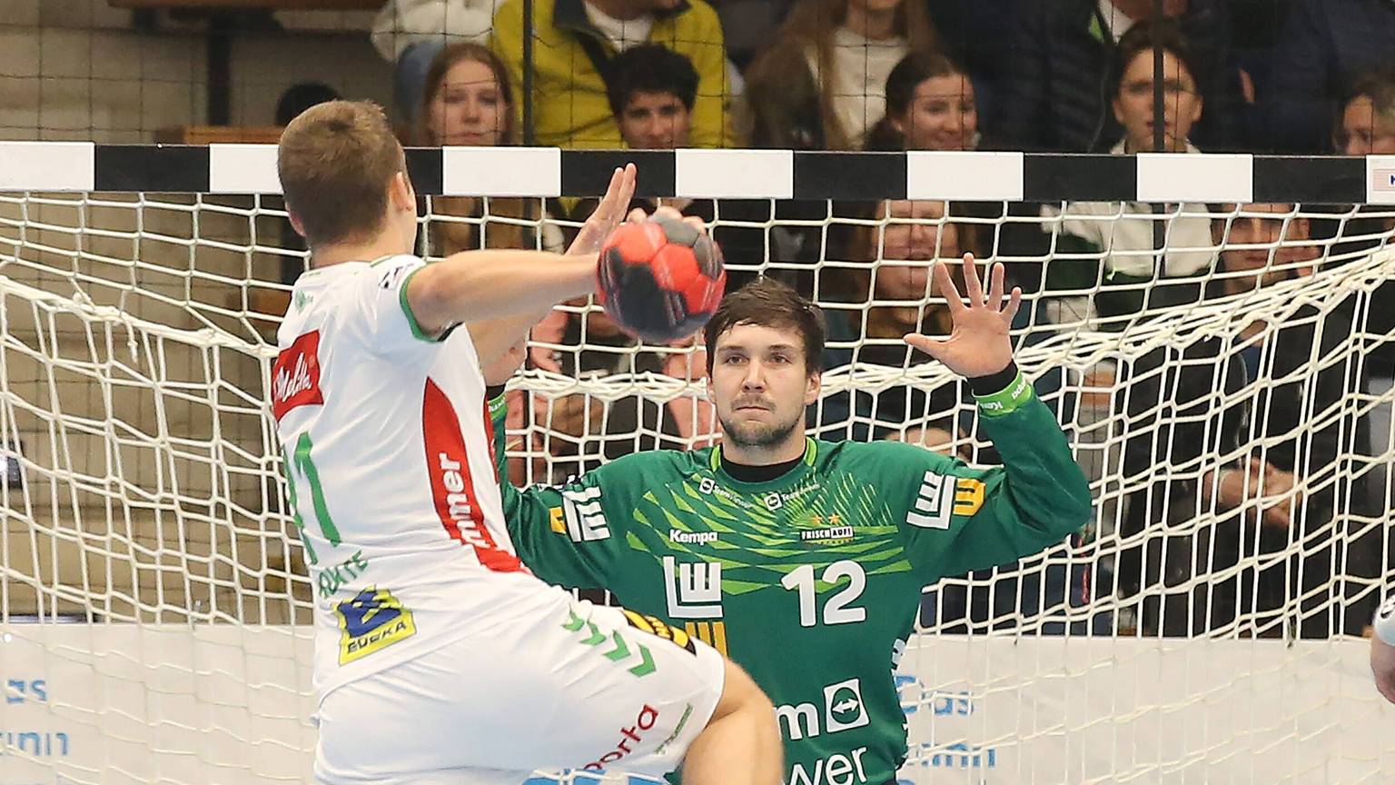 Ein Handballer wird einen Bal aufs Tor, in dem Daniel Rebmann mit grünem Trikot steht.
