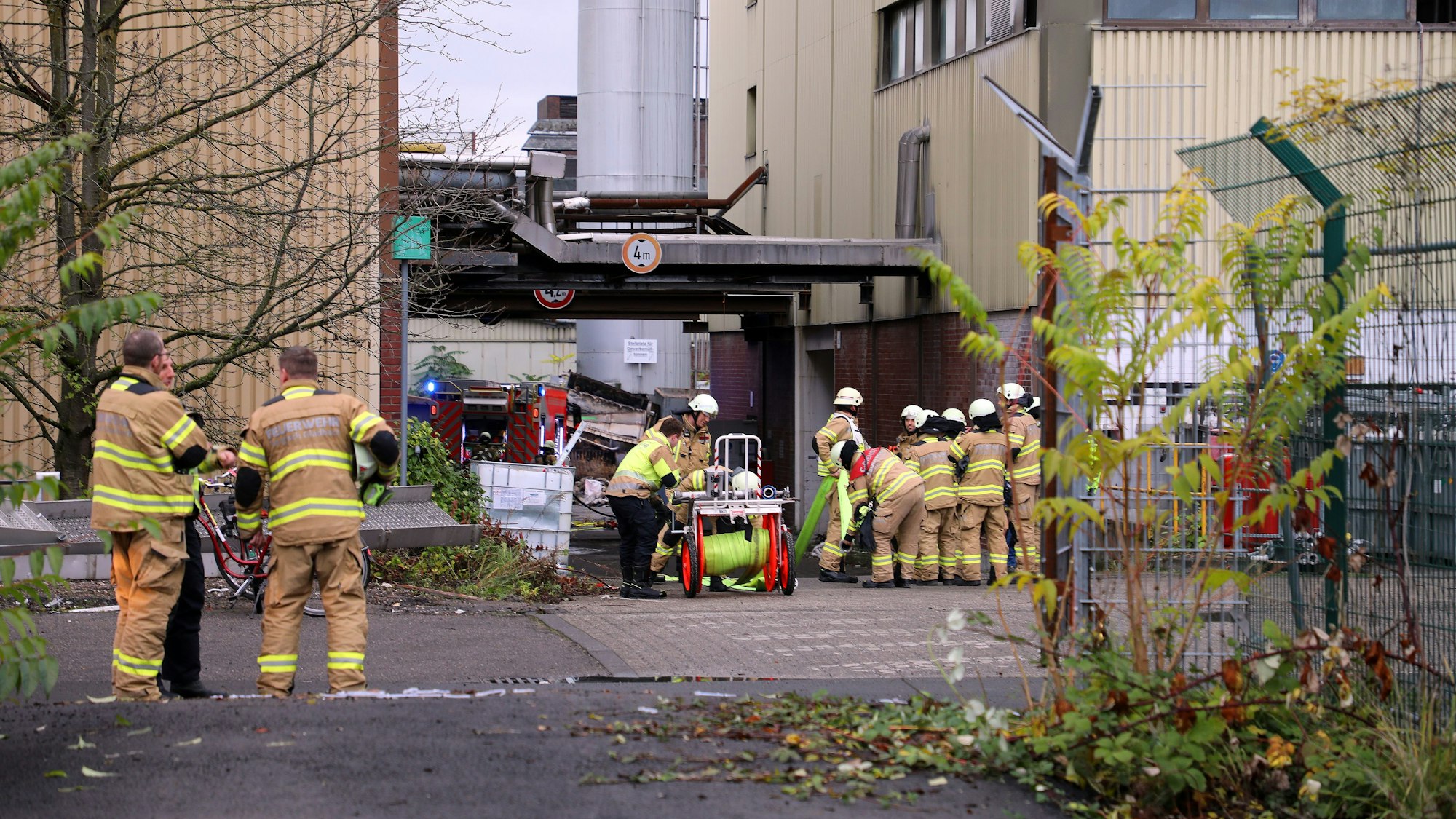 Leute der Feuerwehr stehen vor einem Gebäude. Eine Rolle mit einem Wasserschlauch steht bei ihnen.