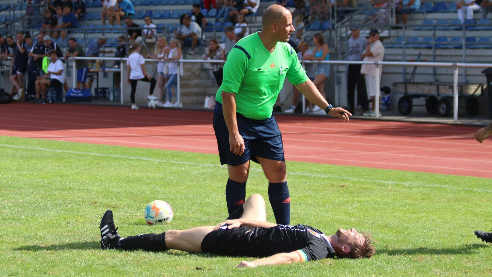 Euskirchens Kapitän Fritz Hilgers liegt auf dem Rasen des Erftstadions und hält sich schmerzverzerrt die Leiste. Der Schiedsrichter steht neben ihm und spricht mit den herannahenden Betreuern.