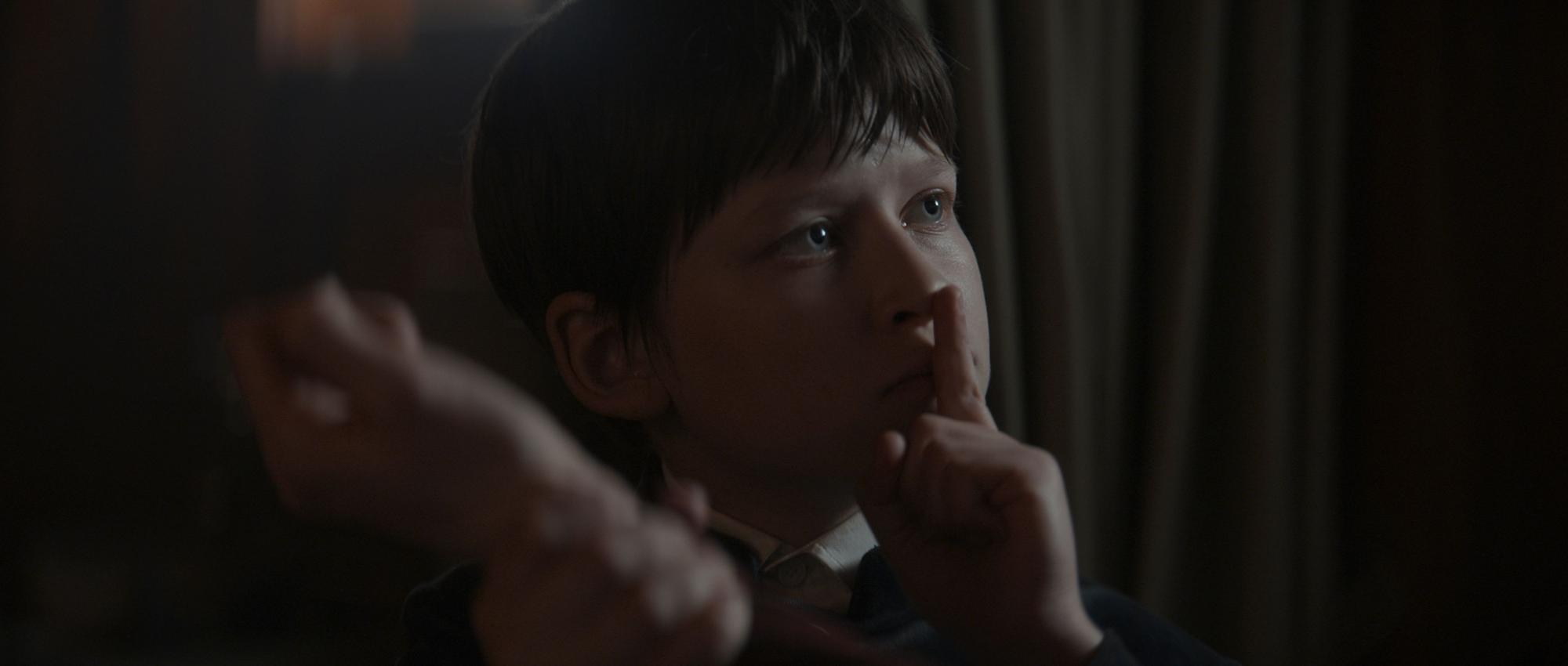 Fflyn Edwards hält den Finger vor den Mund. Der Junge ist in der Netflix-Serie der einzige Überlebende des Geisterschiffs. Er spricht aber nicht.