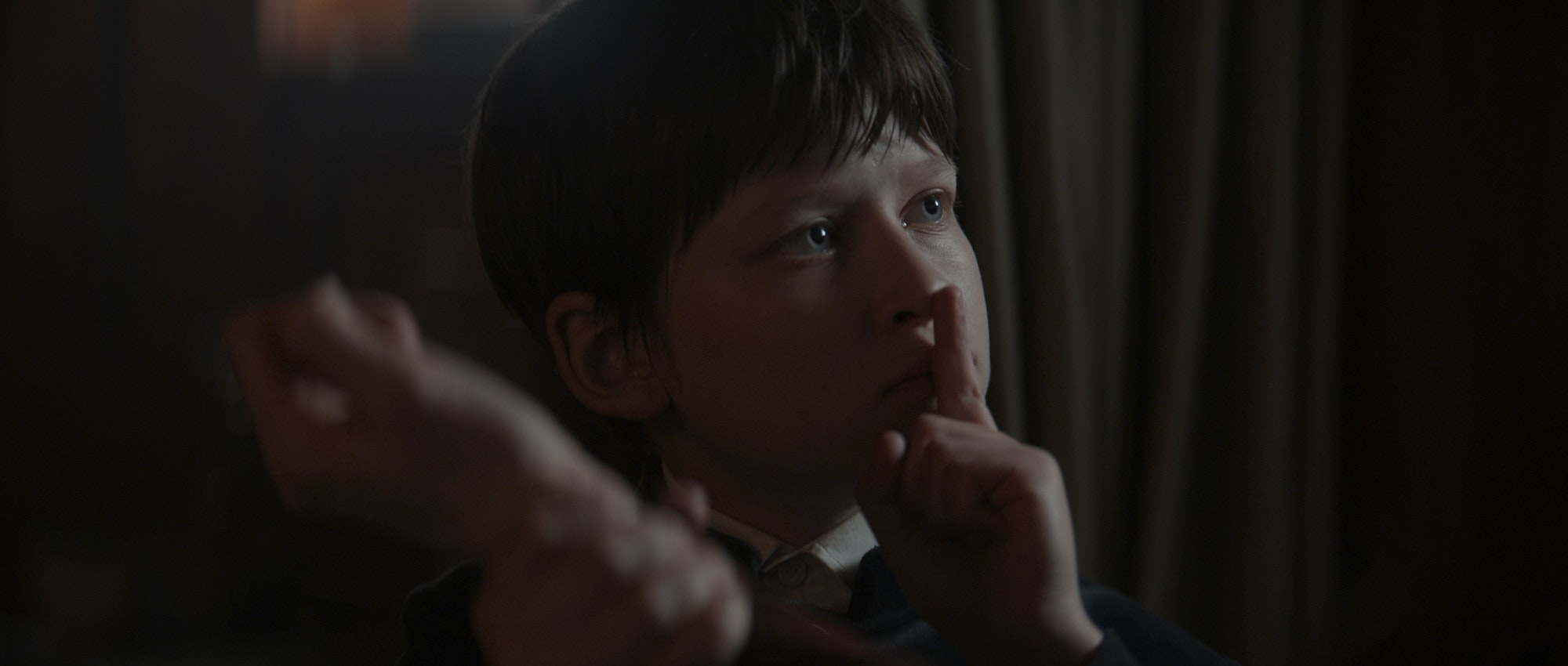 Fflyn Edwards hält den Finger vor den Mund. Der Junge ist in der Netflix-Serie der einzige Überlebende des Geisterschiffs. Er spricht aber nicht.
