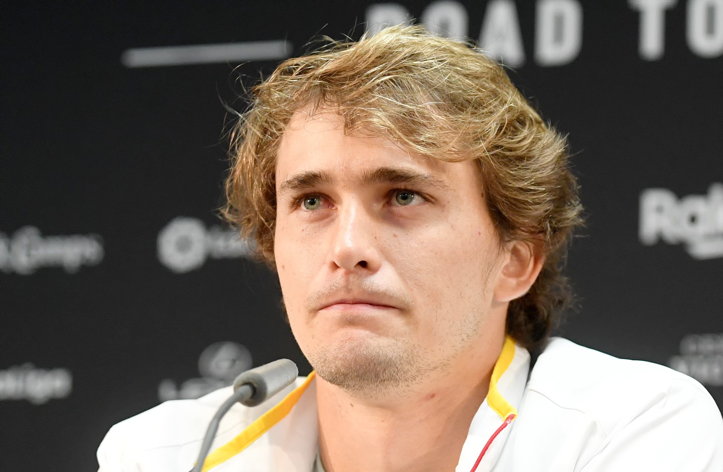 Alexander Zverev sitzt mit ernster Mine vor einem Mikrofon.