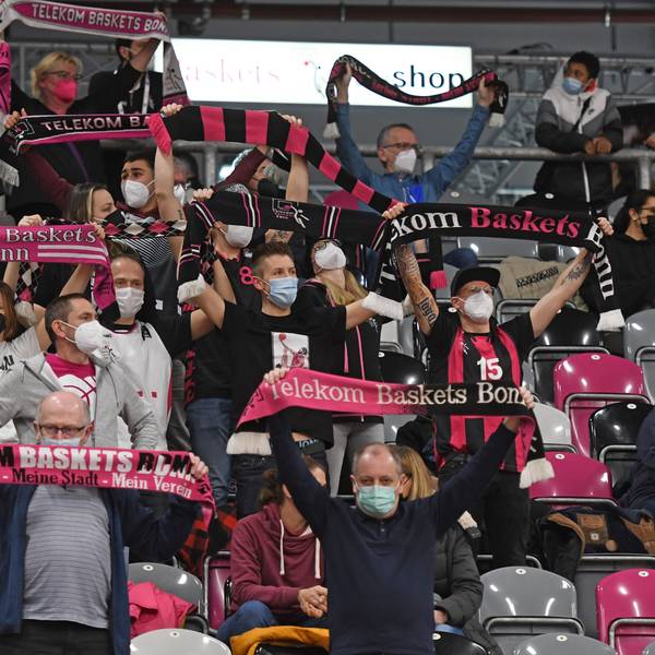 Man sieht die Zuschauertribüne im Stadion, auf ihr sitzen Personen, welche Fanschals der Telekom Baskets hochhalten.