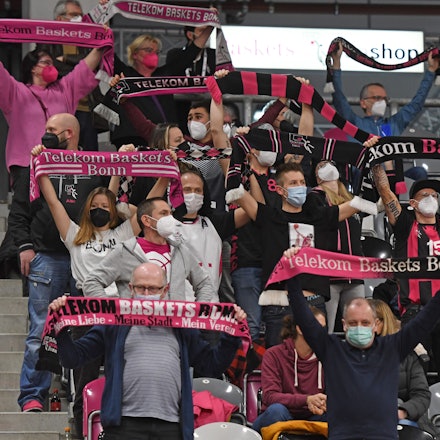 Man sieht die Zuschauertribüne im Stadion, auf ihr sitzen Personen, welche Fanschals der Telekom Baskets hochhalten.
