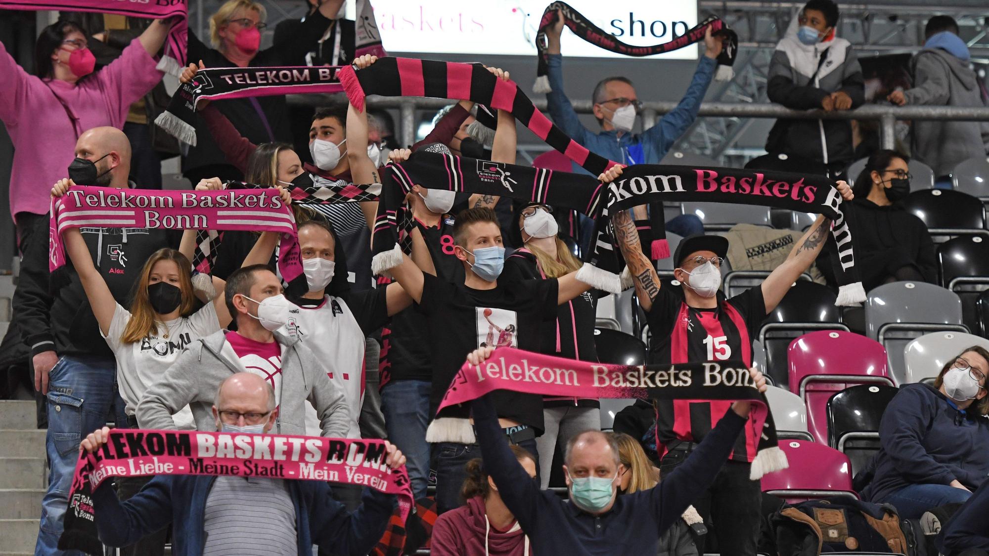 Man sieht die Zuschauertribüne im Stadion, auf ihr sitzen Personen, welche Fanschals der Telekom Baskets hochhalten.