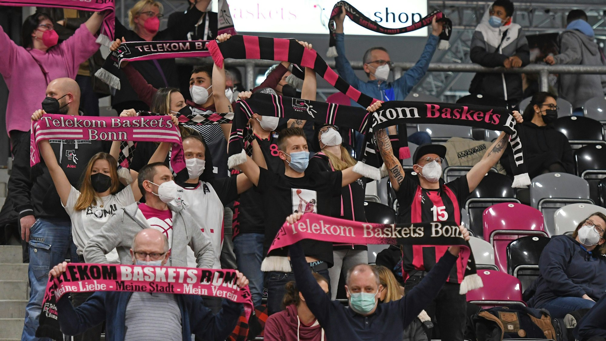 Man sieht die Zuschauertribüne im Stadion, auf ihr sitzen Personen, welche Fanschals der Telekom Baskets hochhalten.
