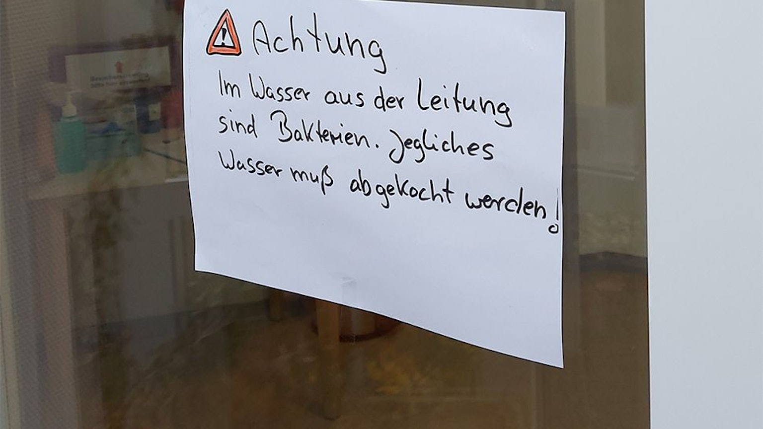 Auf einem Zettel auf einer Glasscheibe steht der Hinweis, dass das Trinkwasser abgekocht werden muss.