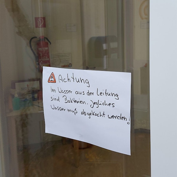 Auf einem Zettel auf einer Glasscheibe steht der Hinweis, dass das Trinkwasser abgekocht werden muss.