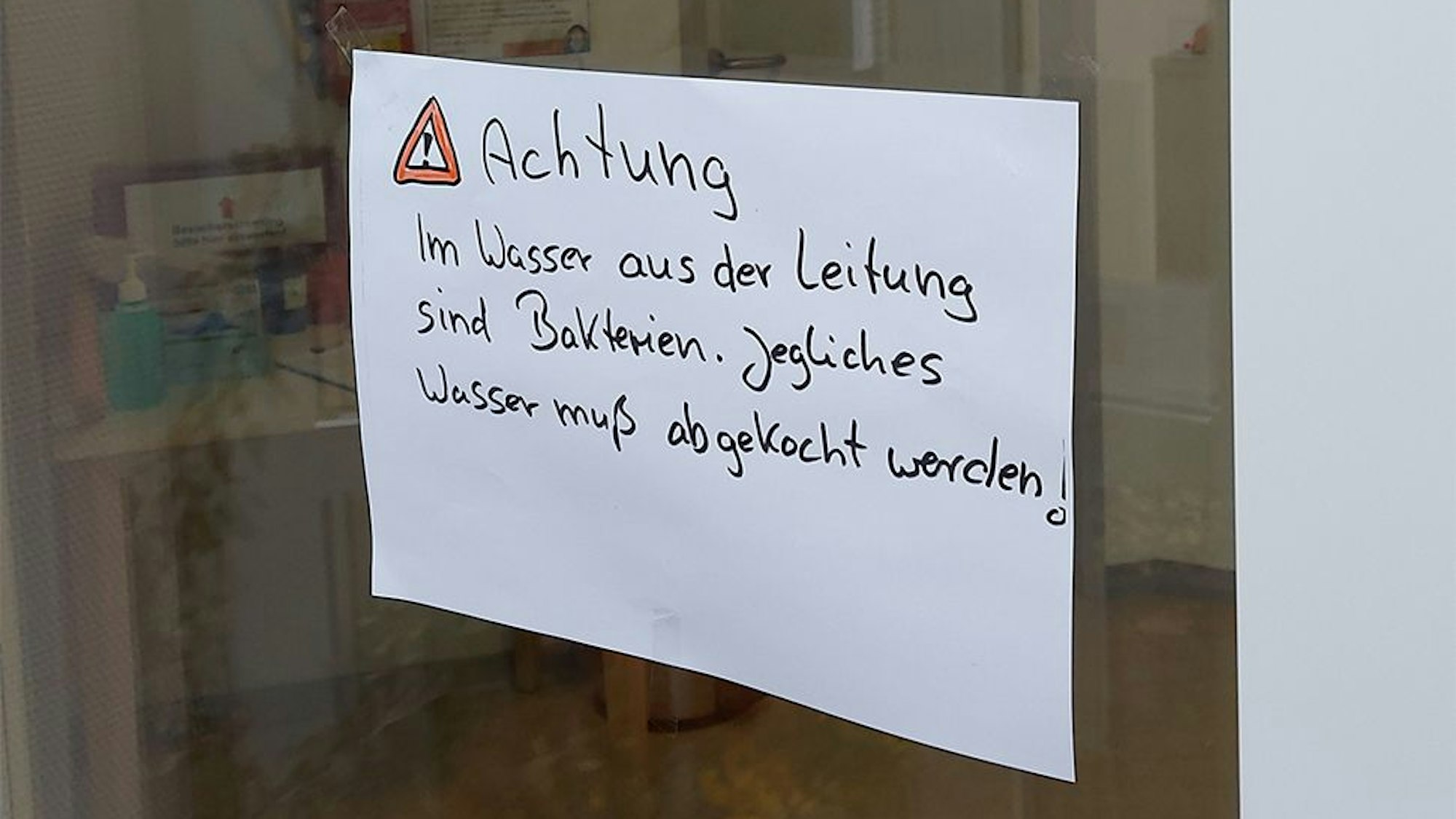 Auf einem Zettel auf einer Glasscheibe steht der Hinweis, dass das Trinkwasser abgekocht werden muss.