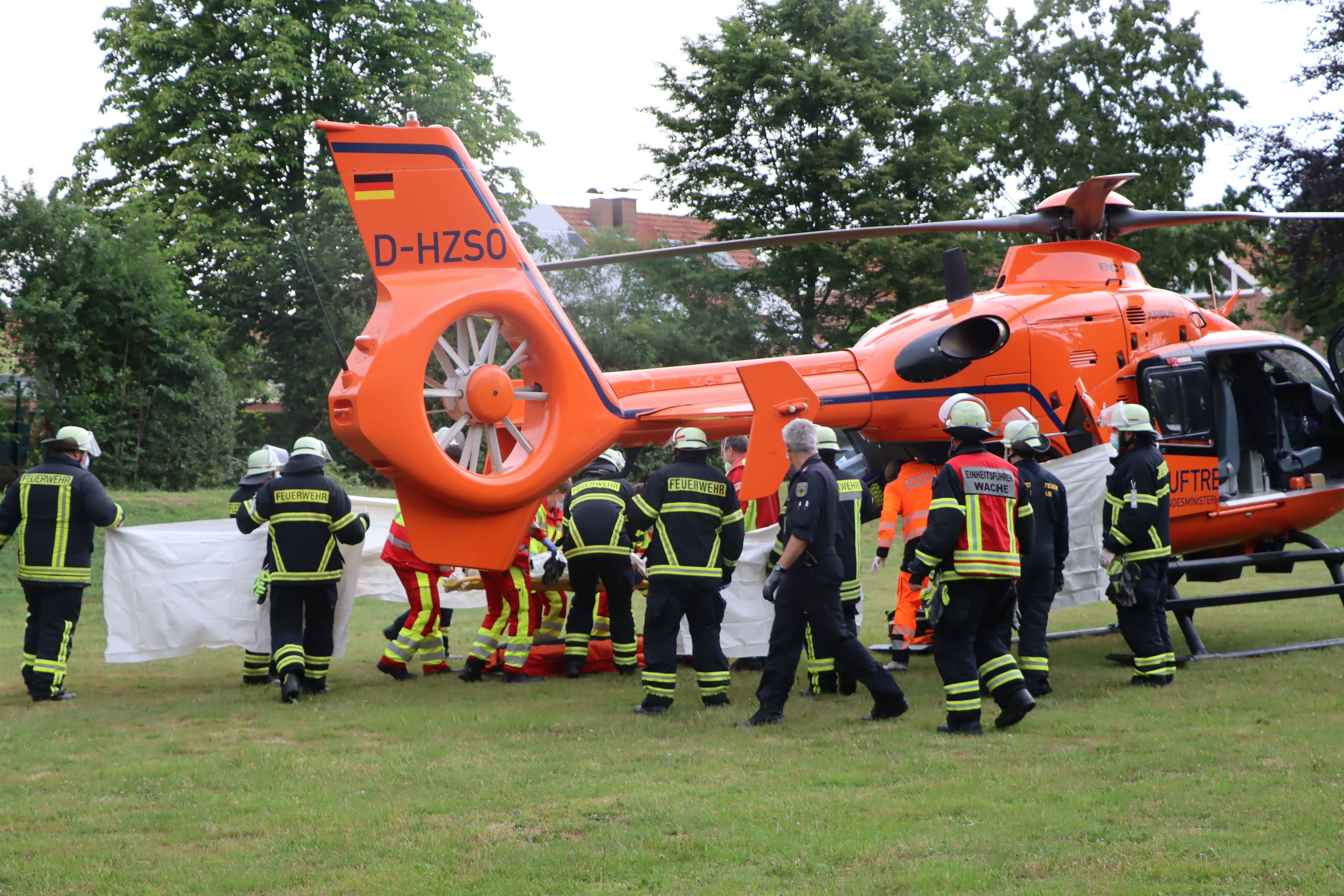 Feuerwehrleute und Rettungssanitäter stehen vor einem Rettungshubschrauber.