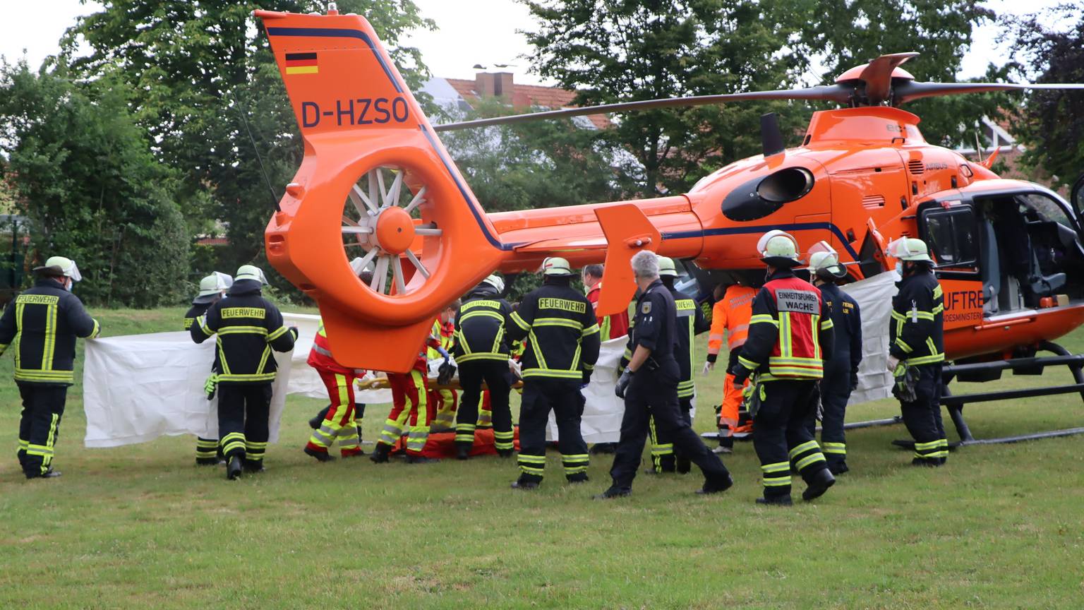 Feuerwehrleute und Rettungssanitäter stehen vor einem Rettungshubschrauber.