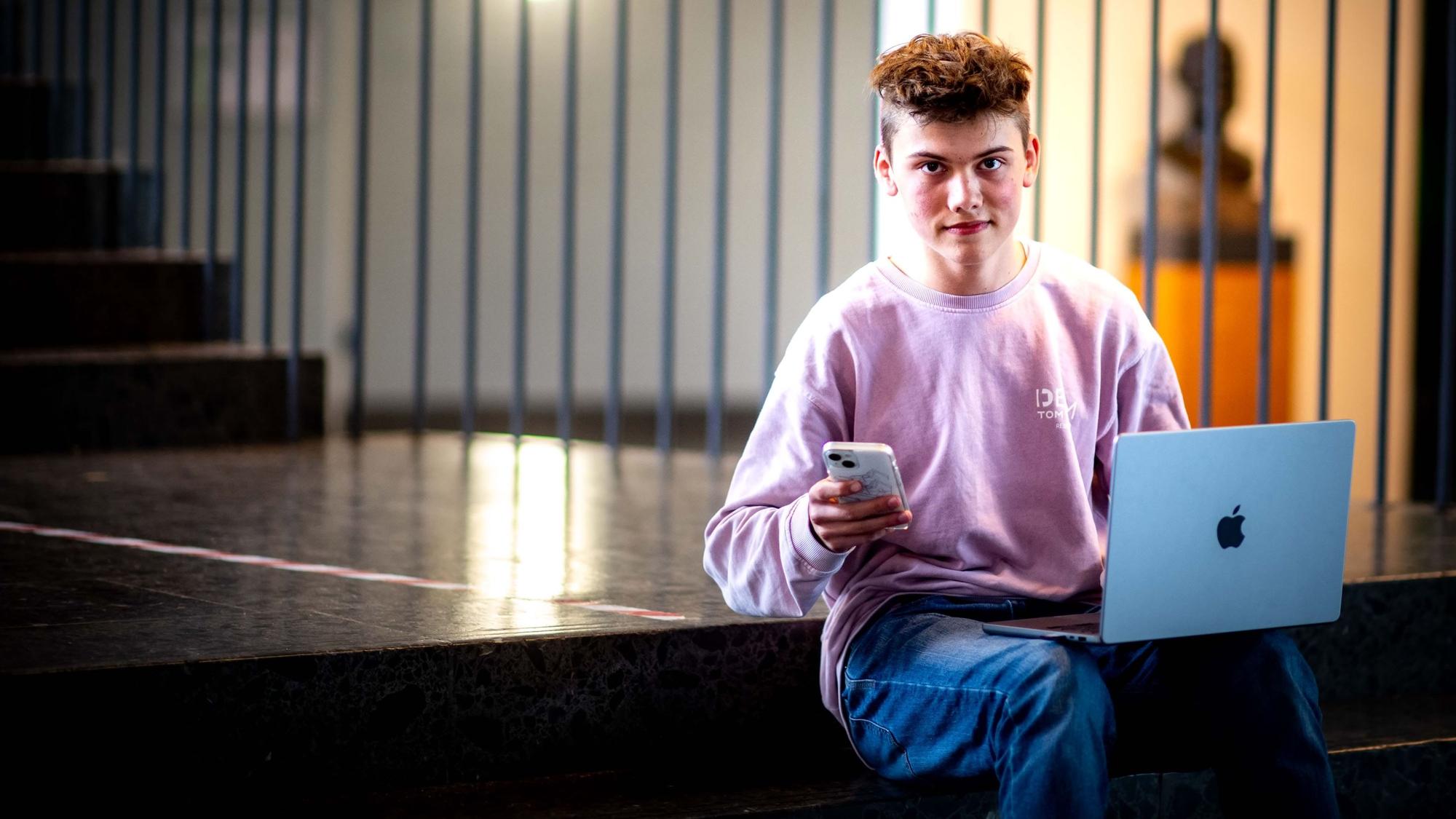 Handy in der Hand, Laptop auf den Beinen. Schüler Noel Dederichs sitzt auf den Stufen des Emil-Fischer-Gymnasiums in Euskirchen.