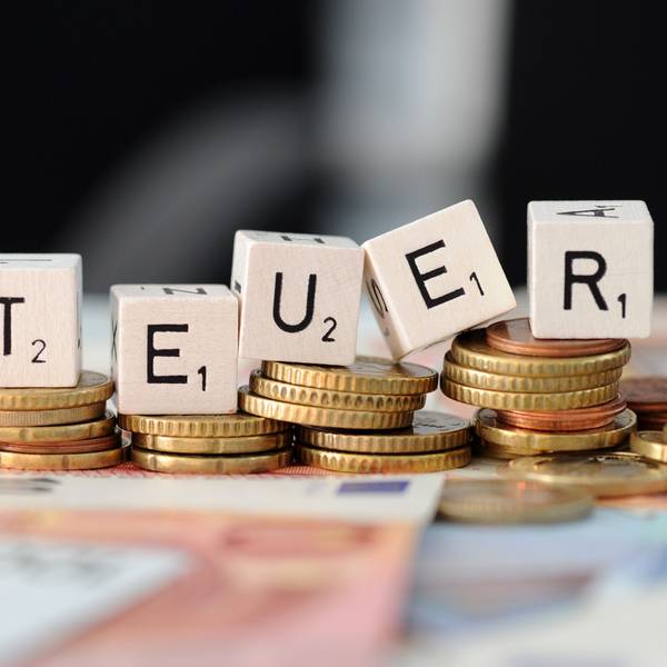 Würfel mit den Buchstaben S t e u e r liegen auf Geldmünzen und Geldscheinen.
