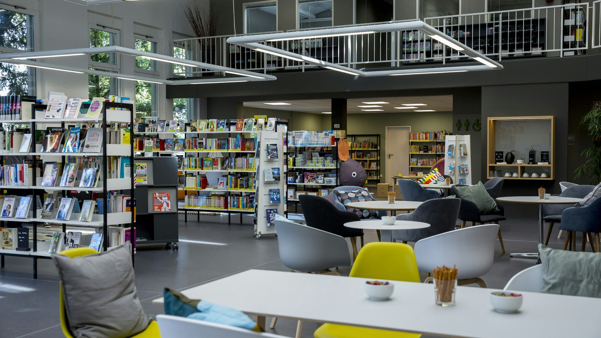 In einem Raum stehen Bücherregale und Tische mit Stühlen wie in einem Café.
