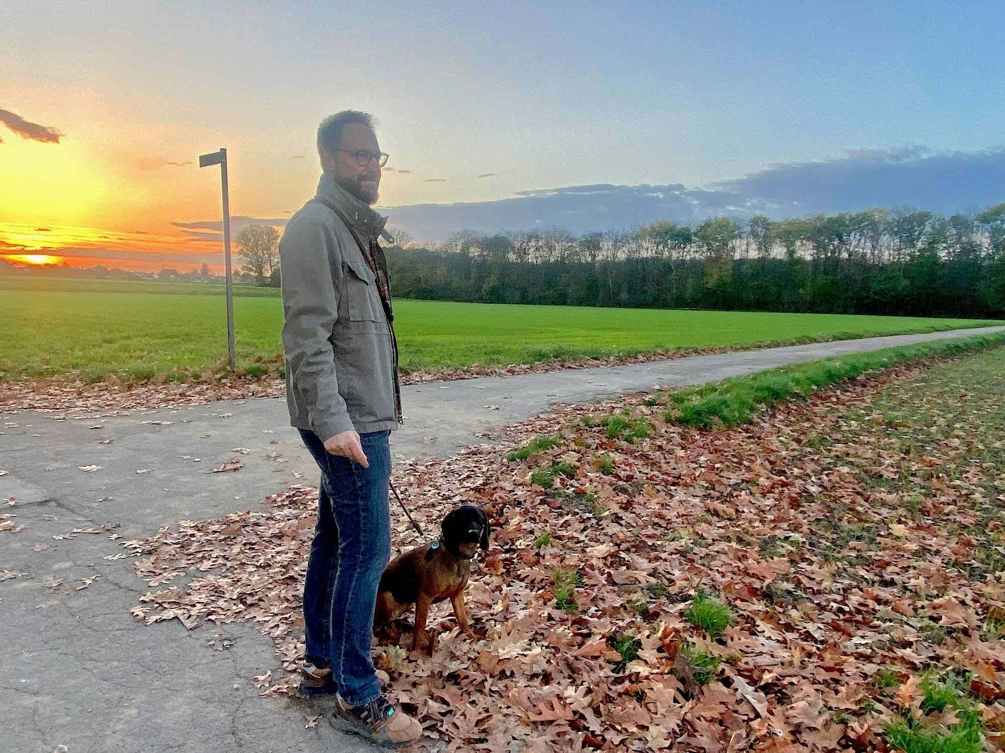 Ein Mann blickt auf ein Feld, sein Hund sitzt neben ihm.