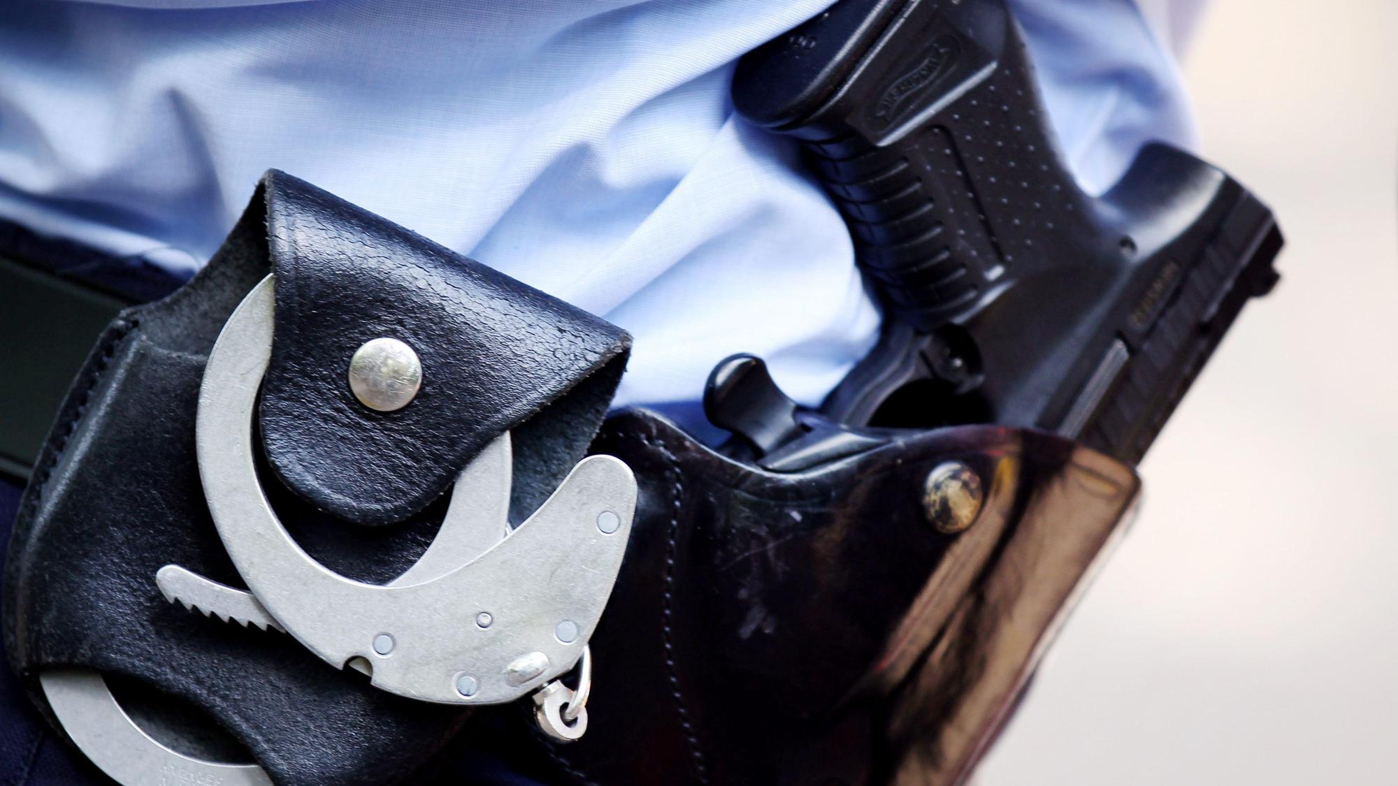 Ein Polizist mit Handschellen und Pistole am Gürtel steht auf der Straße.
