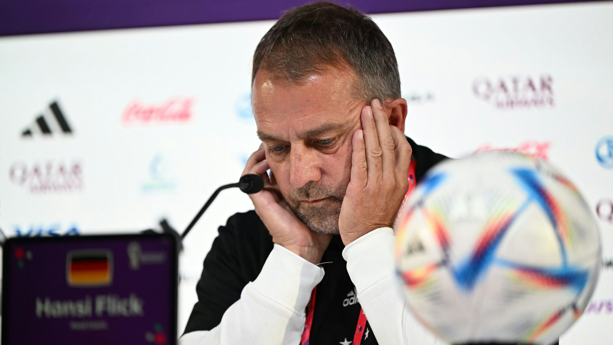 Bundestrainer Hansi Flick gibt eine Pressekonferenz. Er blickt sorgenvoll auf den Tisch, an dem er sitzt. Ein Mikrofon ist auf ihn gerichtet.