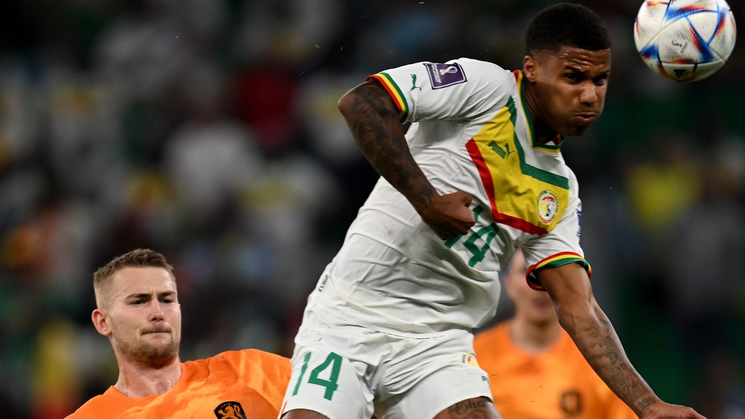 Ein Fußballspieler springt in einem Zweikampf gegen einen anderen Spieler und bringt den Ball mit einem Kopfball außer Reichweite des Gegners.