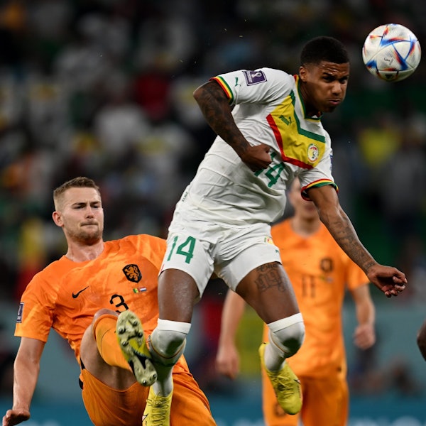 Ein Fußballspieler springt in einem Zweikampf gegen einen anderen Spieler und bringt den Ball mit einem Kopfball außer Reichweite des Gegners.