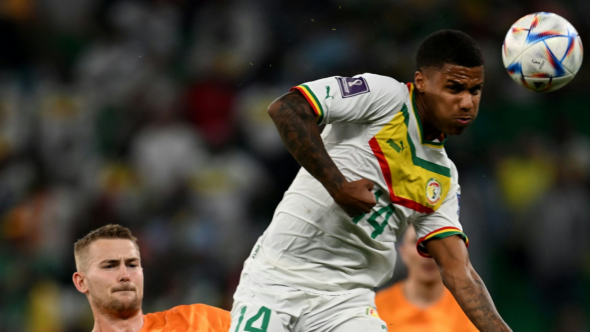 Ein Fußballspieler springt in einem Zweikampf gegen einen anderen Spieler und bringt den Ball mit einem Kopfball außer Reichweite des Gegners.