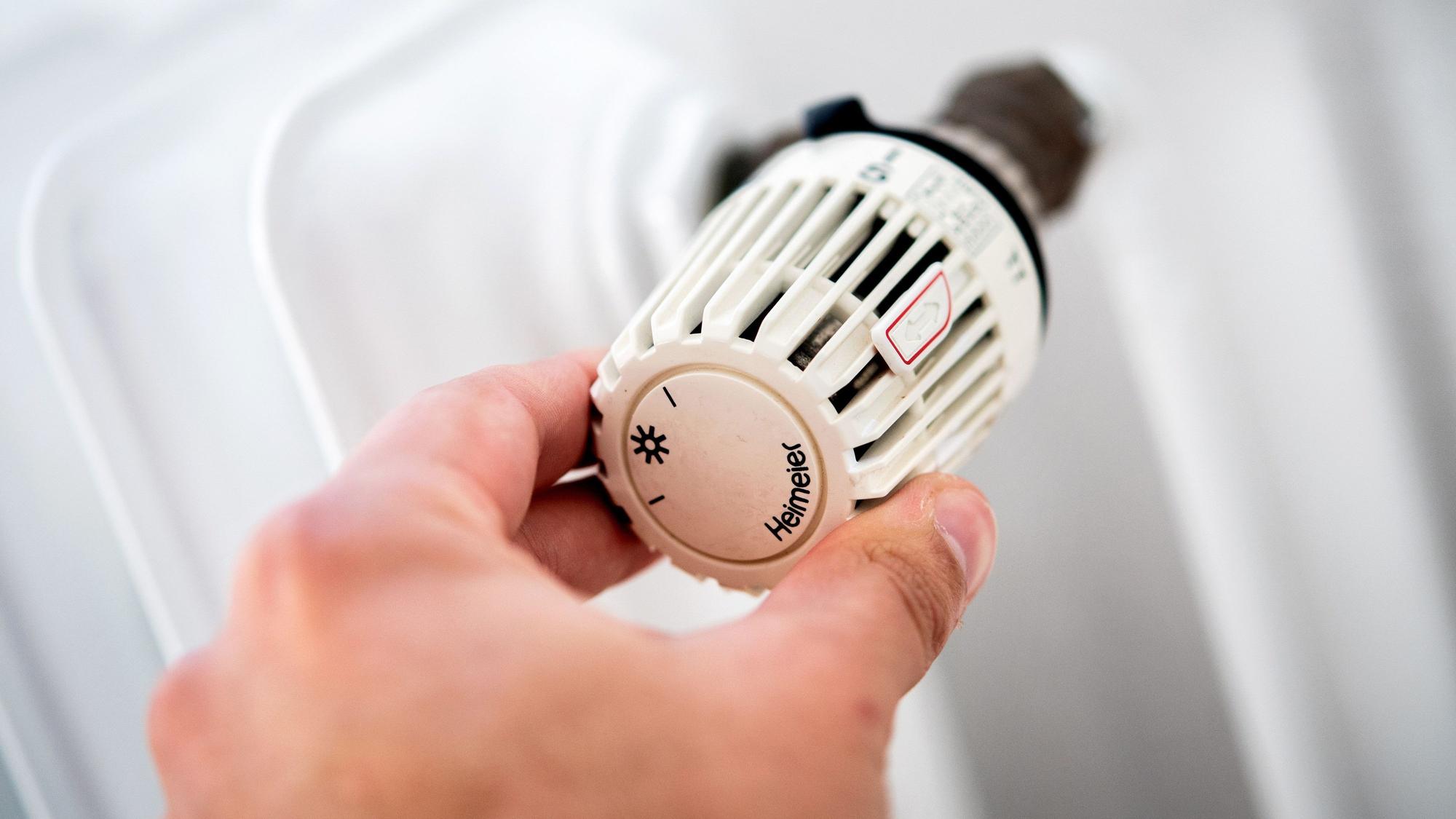 Ein Mann dreht in einer Wohnung am Thermostat einer Heizung.