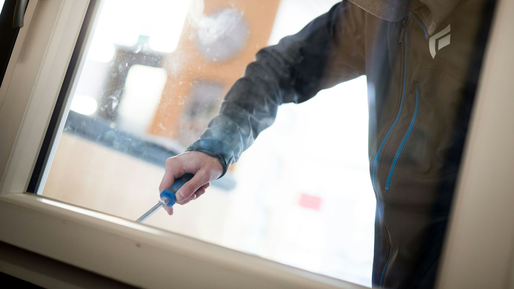Ein Einbrecher macht sich mit einem Schraubenzieher an einem Fenster zu schaffen.