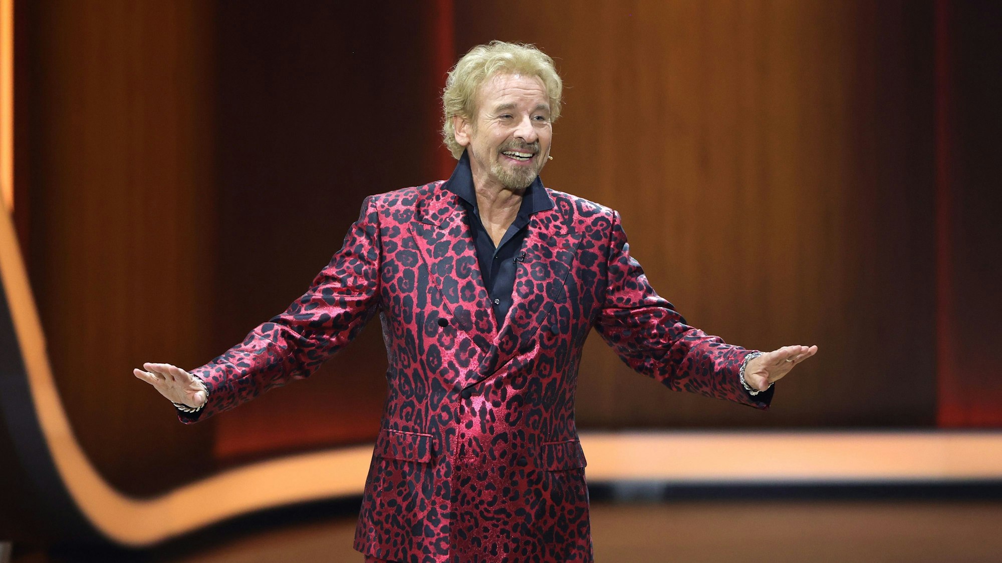 Thomas Gottschalk steht auf der Bühne und spricht in die Kamera. Er trägt einen bordeauxfarbenen Anzug in Leoparden-Print.