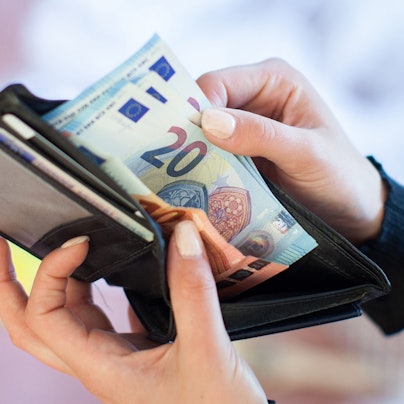 Eine Frau nimmt Banknoten aus einem Geldbeutel.