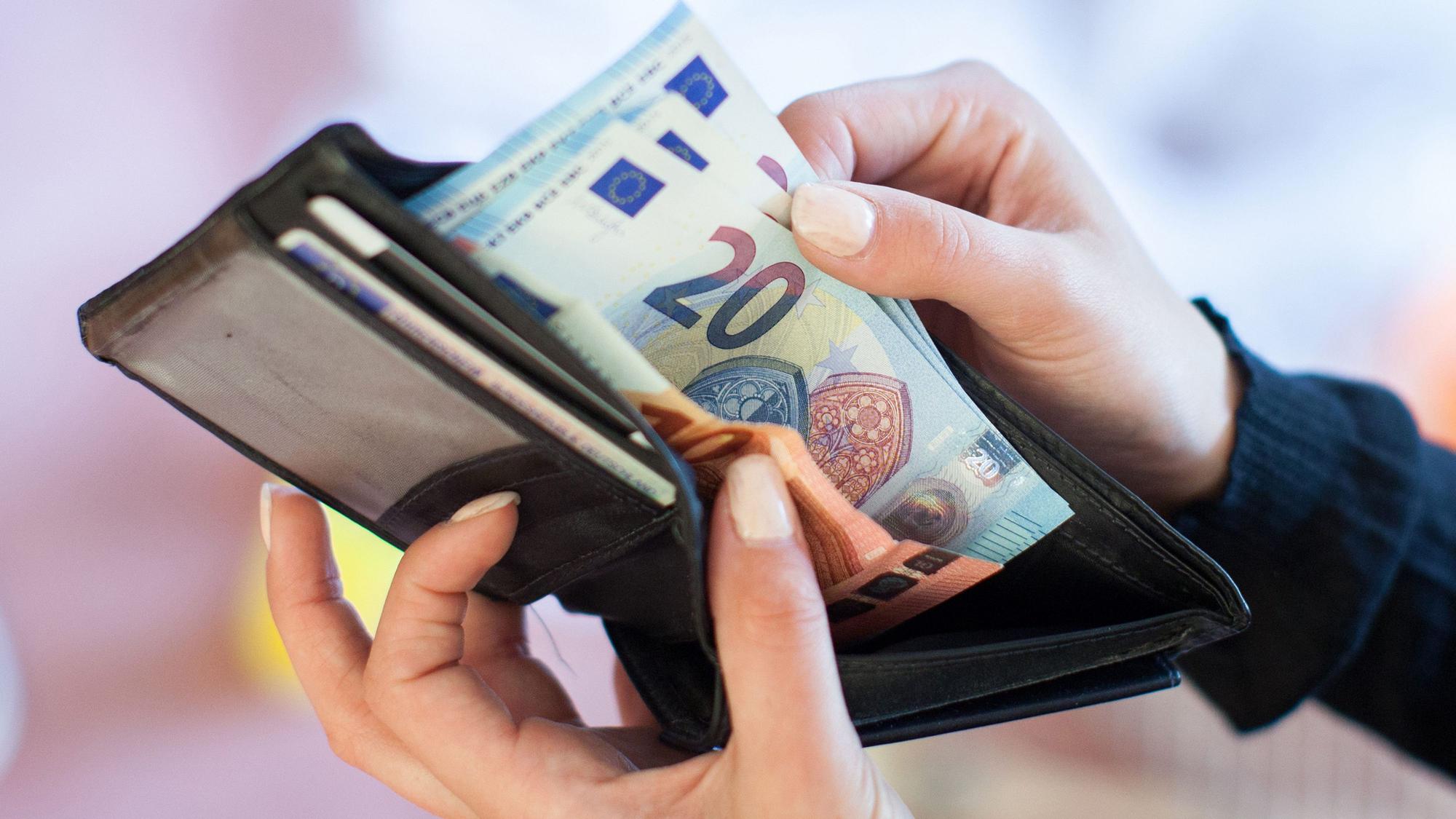 ILLUSTRATION - Eine Frau nimmt Banknoten aus einem Geldbeutel.