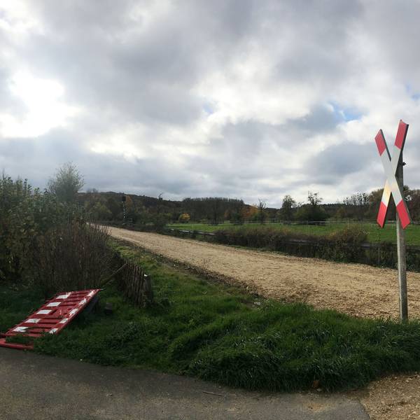 Auf der Bahnstrecke liegen keine Gleise. Neben der Strecke liegt ein Haus. Davor stehen Autos.