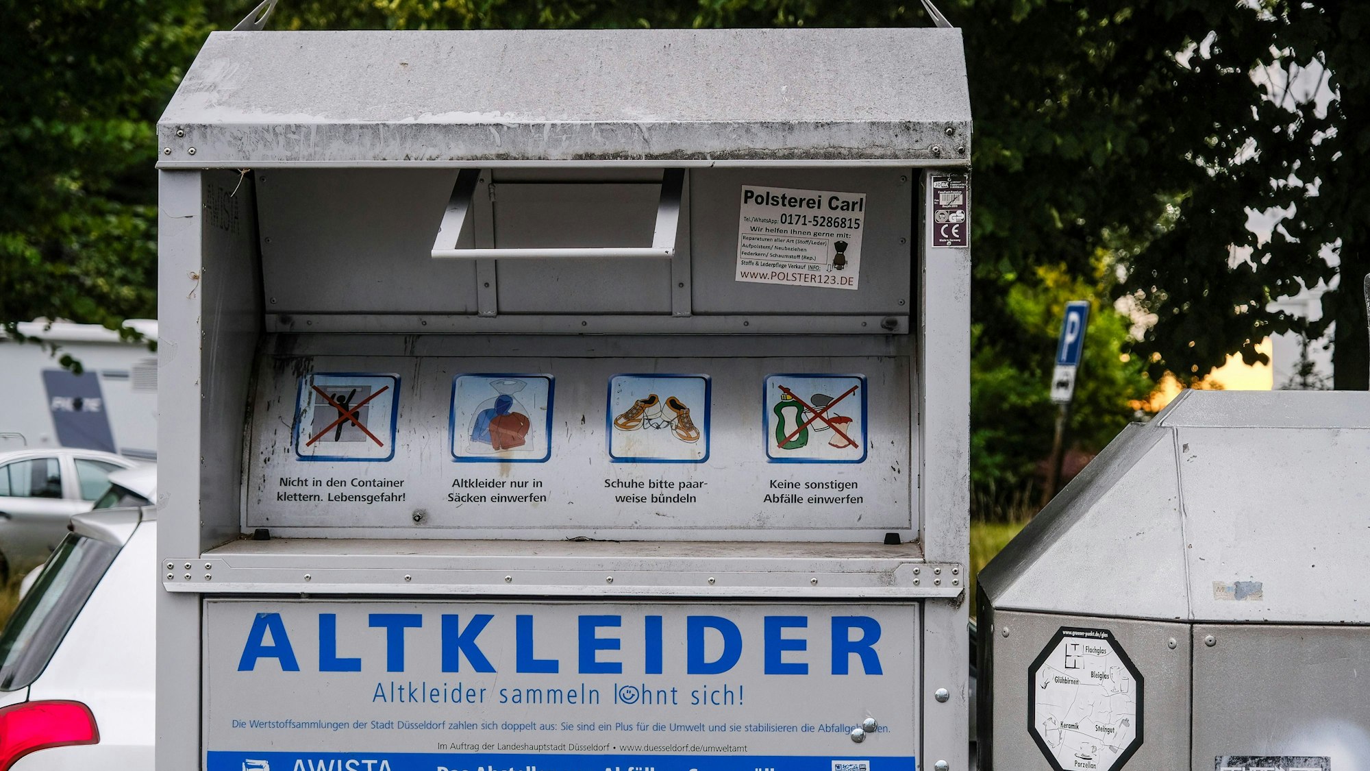 Ein silberner Altkleider-Container steht an einem Parkplatz.