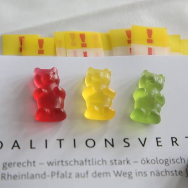 ILLUSTRATION - Ein rotes, ein gelbes und ein grünes Gummibärchen liegen auf dem Exemplar eines Koalitionsvertrages.