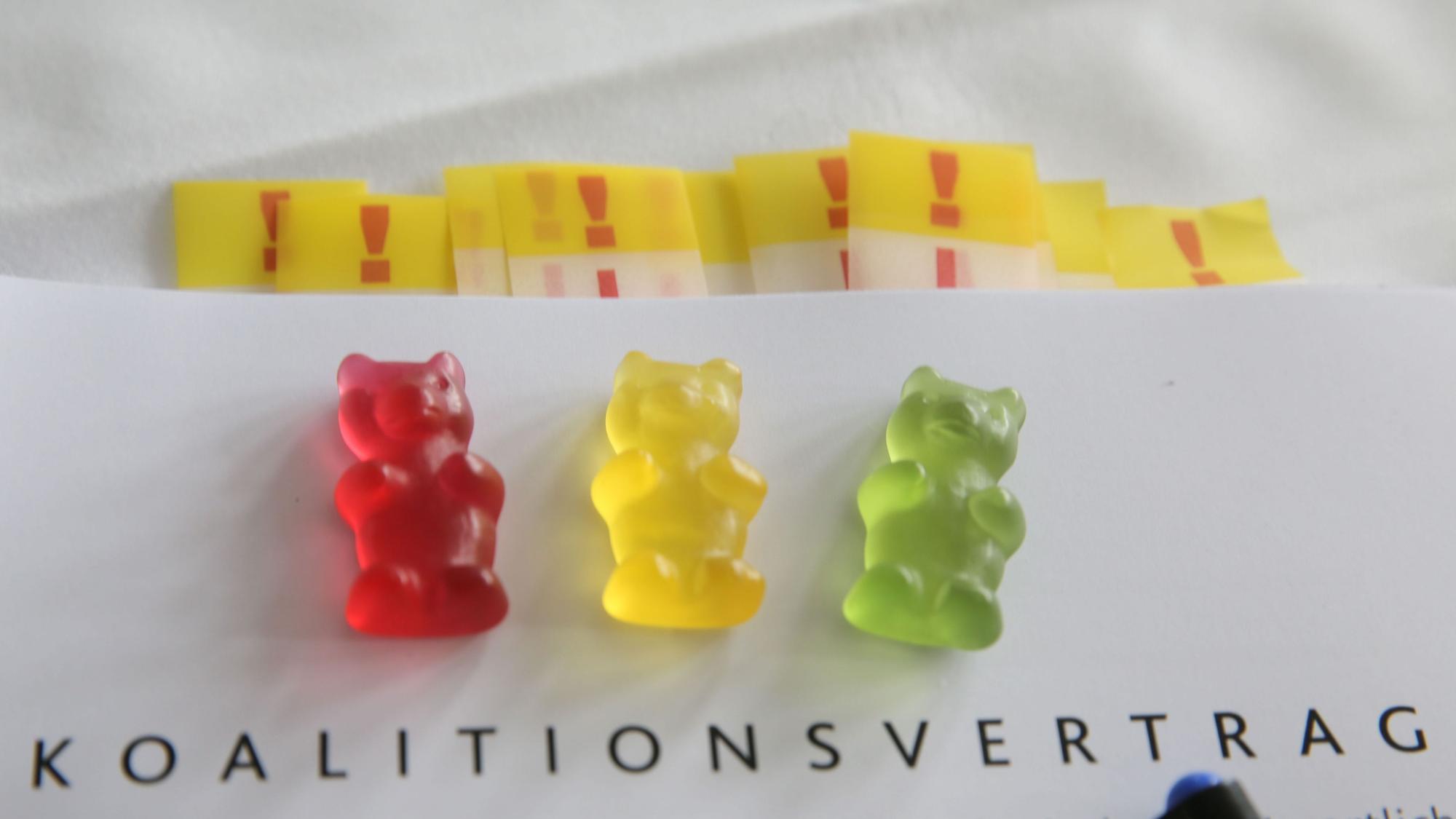 ILLUSTRATION - Ein rotes, ein gelbes und ein grünes Gummibärchen liegen auf dem Exemplar eines Koalitionsvertrages.