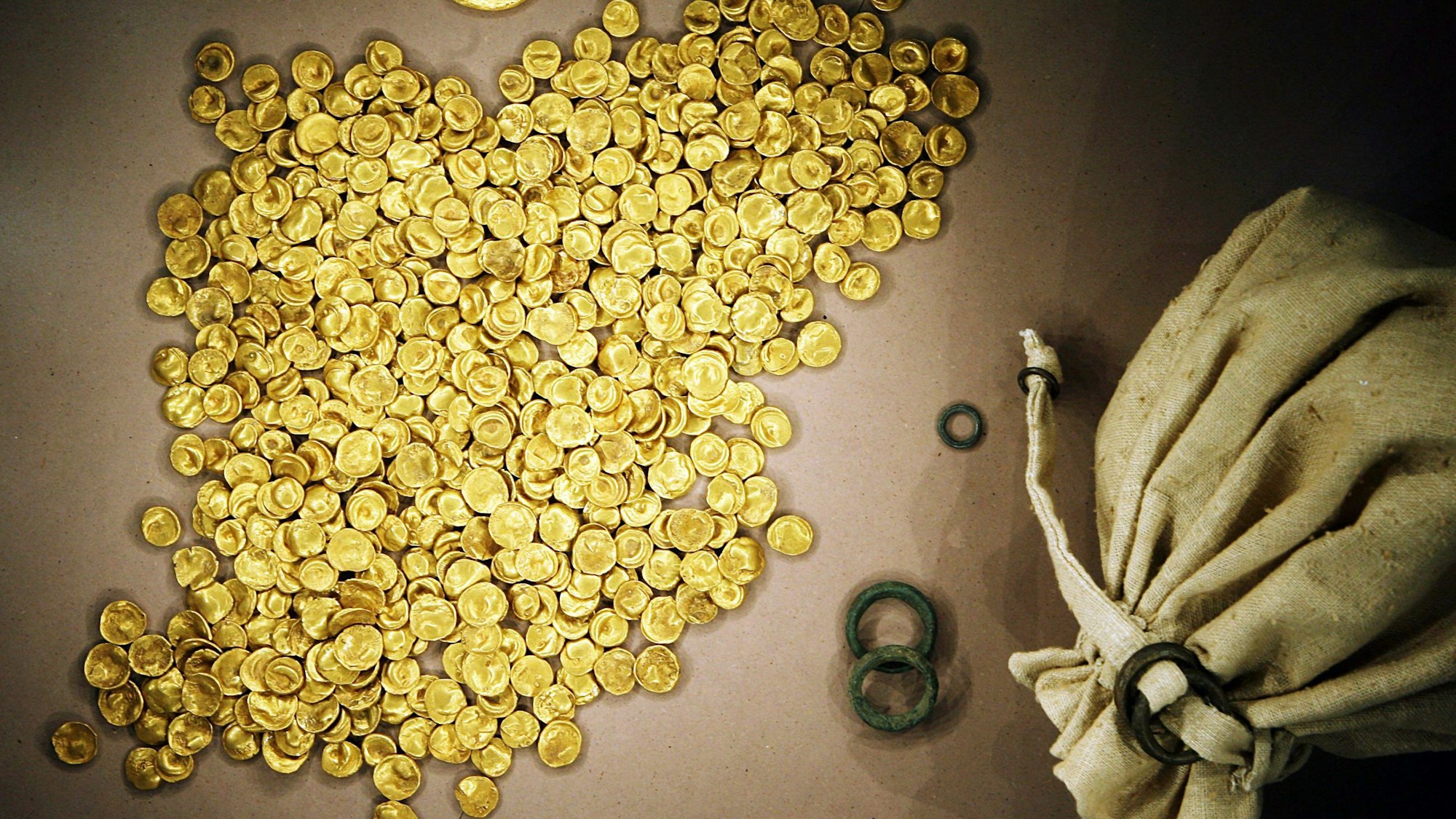 Viele Goldmünzen und ein Säckchen als Behälter sind zu sehen, die Münzen strahlen leuchtend-gold.