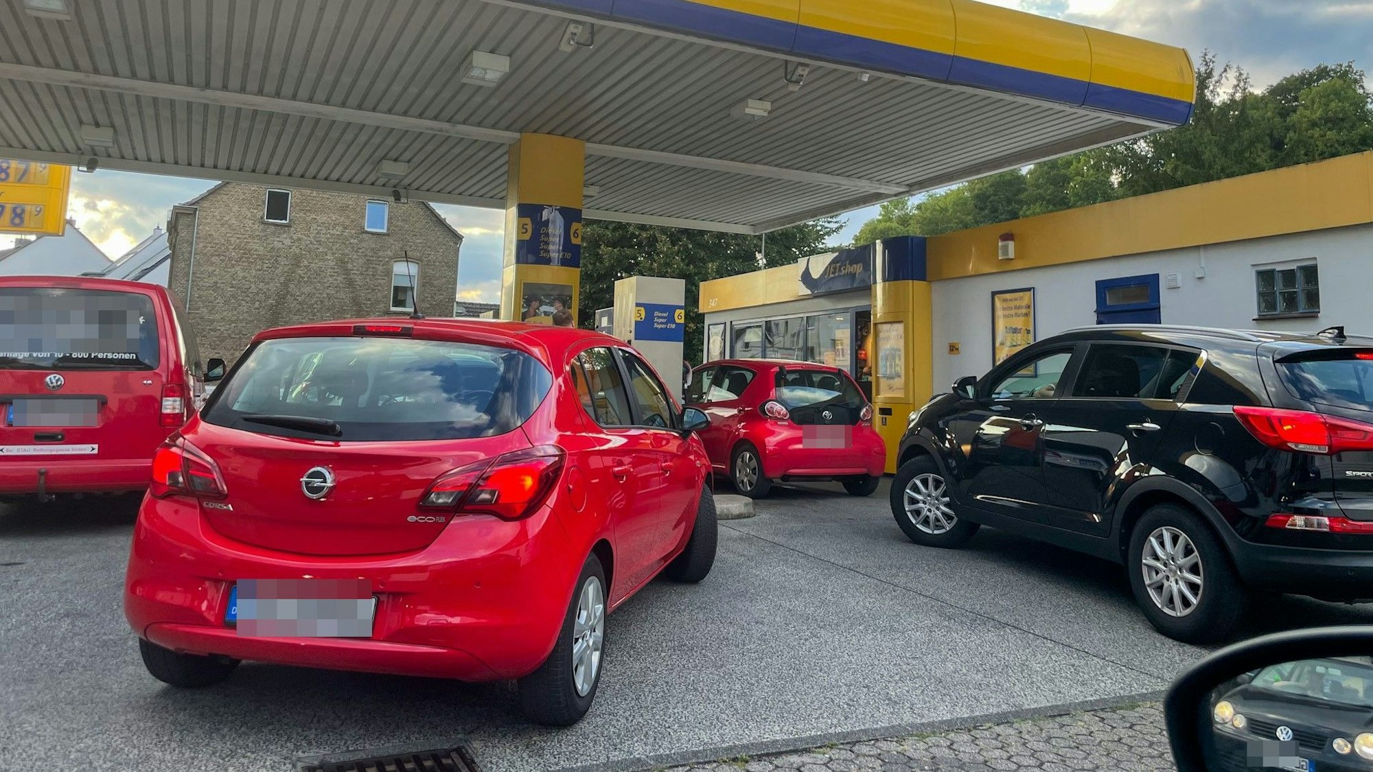 Drei rote und ein schwarzes Auto warten an einer Tankstelle in Bergisch Gladbach.