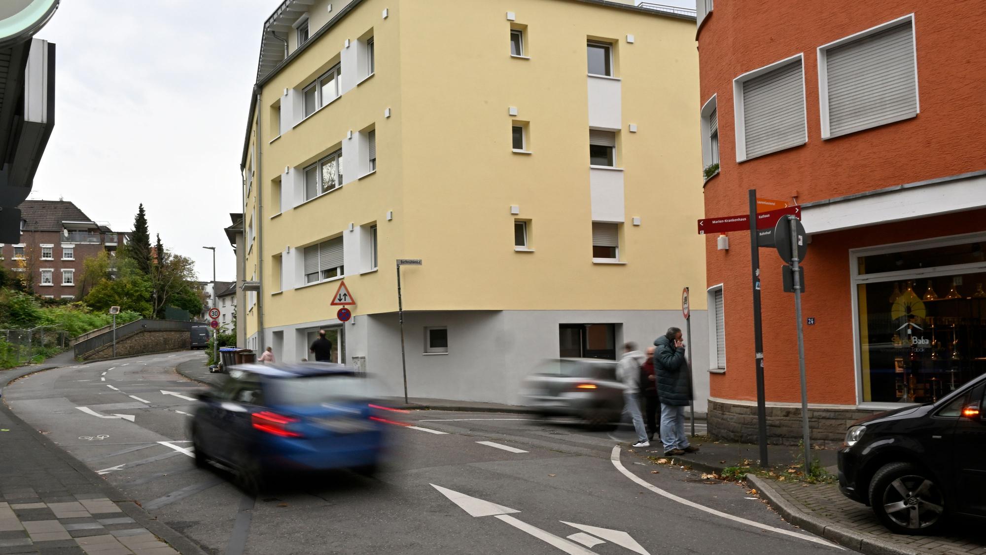 Ein blaues Auto fährt auf der Laurentiusstraße, auf dem Bürgersteig stehen Passanten.